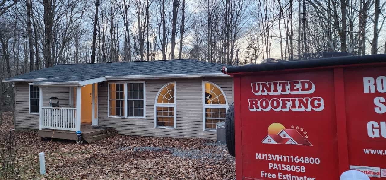 A house next to a red United Roofing truck in a wooded area. The house has windows and a porch.