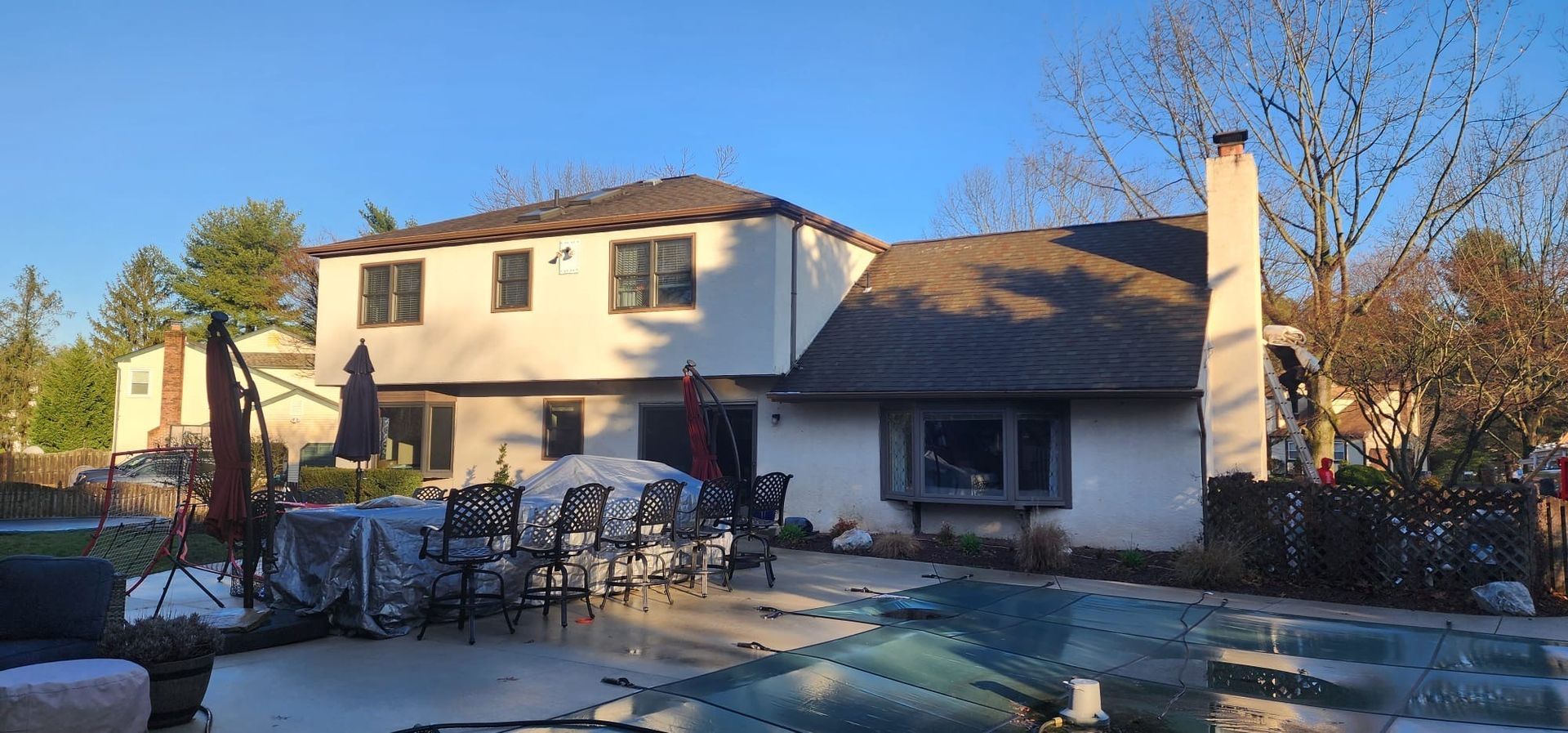 Backyard view of a house with a pool, patio furniture, and trees under a clear blue sky.