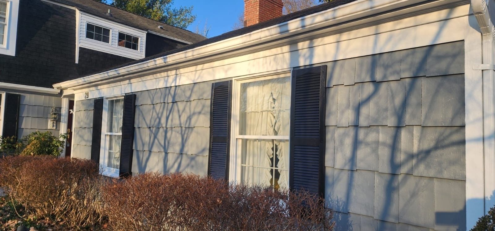Exterior of a house with grey siding, white trim, black shutters, and a chimney.