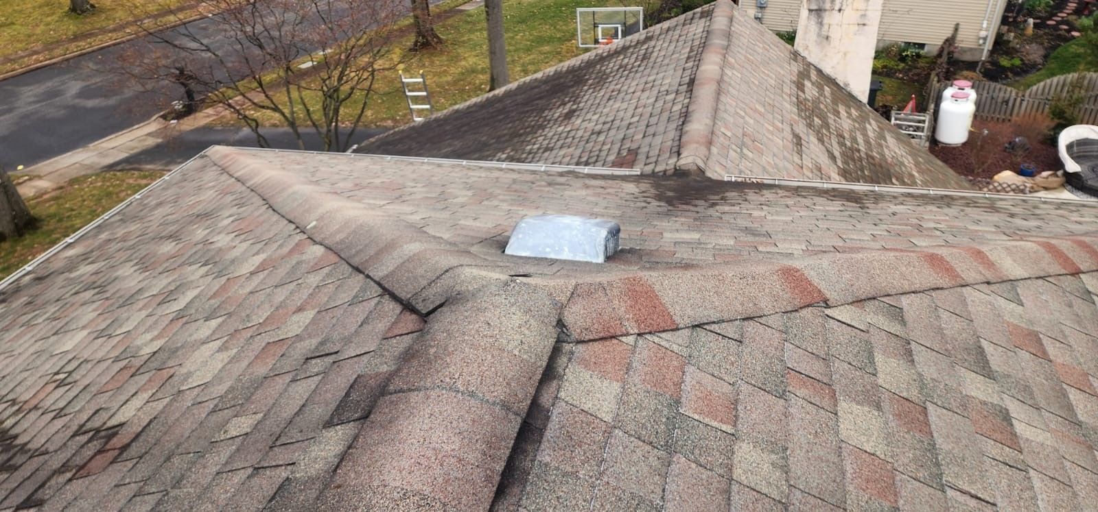 View of an asphalt shingle roof with a metal vent. Brown and red shingles. Overcast, outdoor setting.