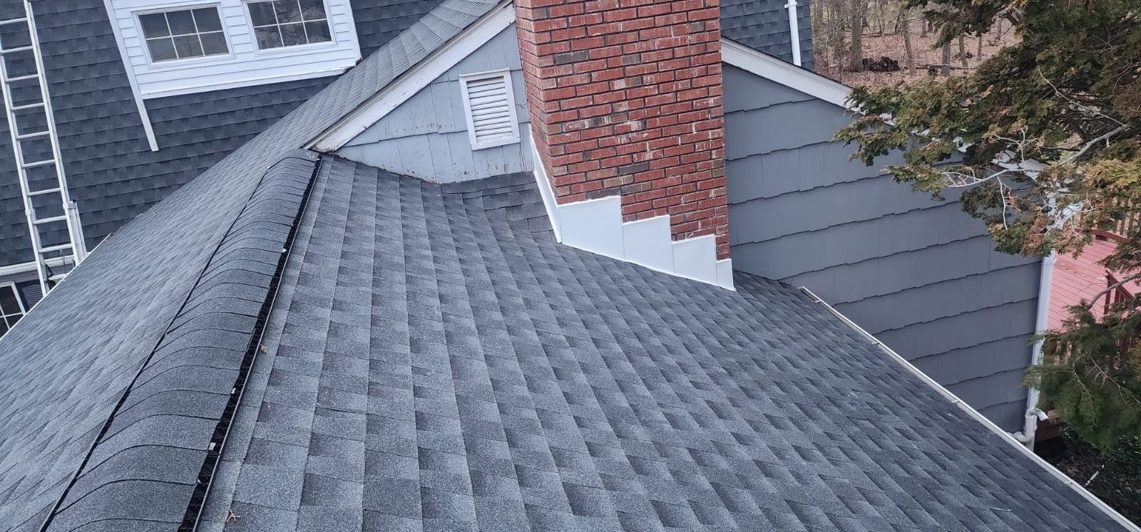 View of a dark gray shingled roof with a red brick chimney.
