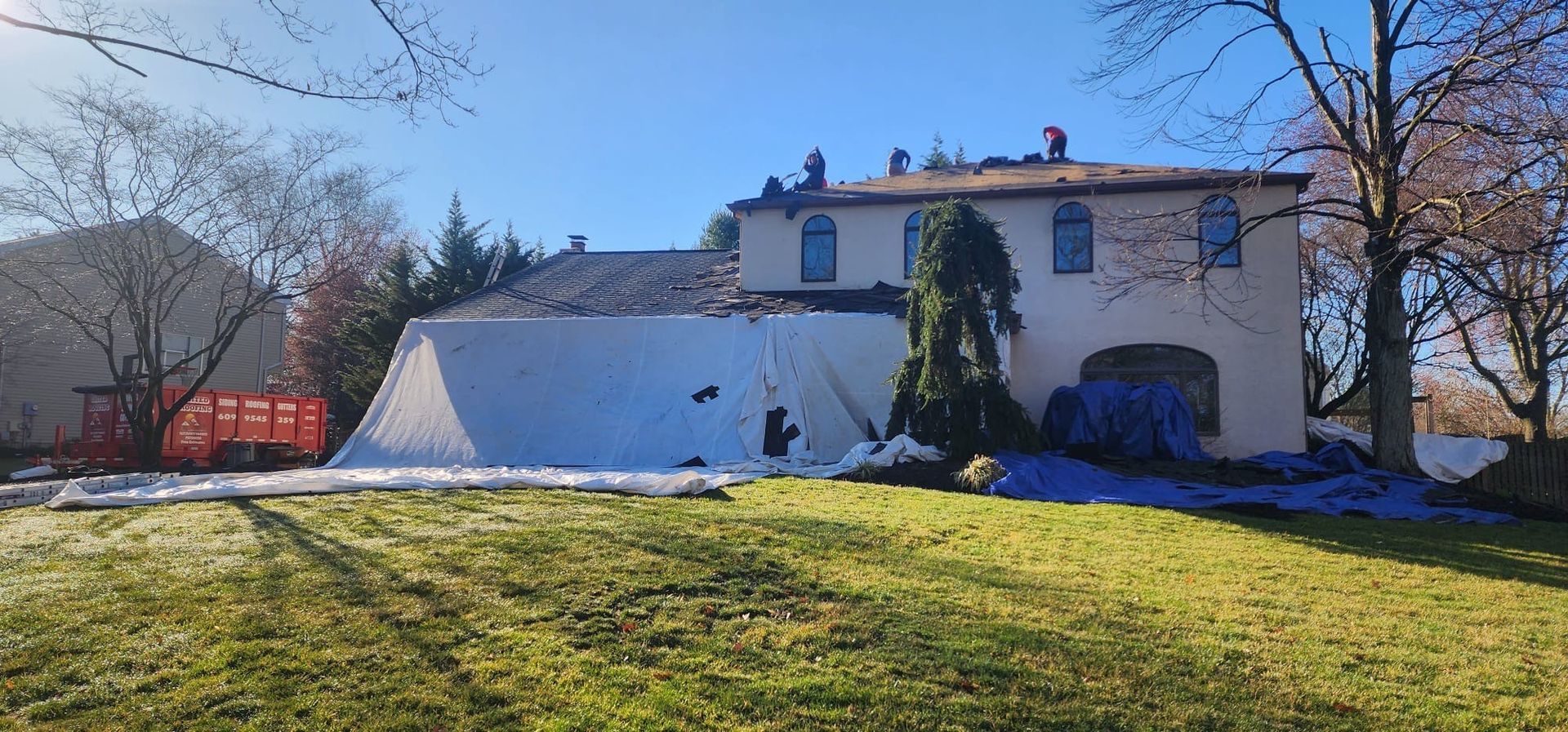 Workers on a rooftop, covered by a blue tarp, on a sunny day. A building is being worked on.