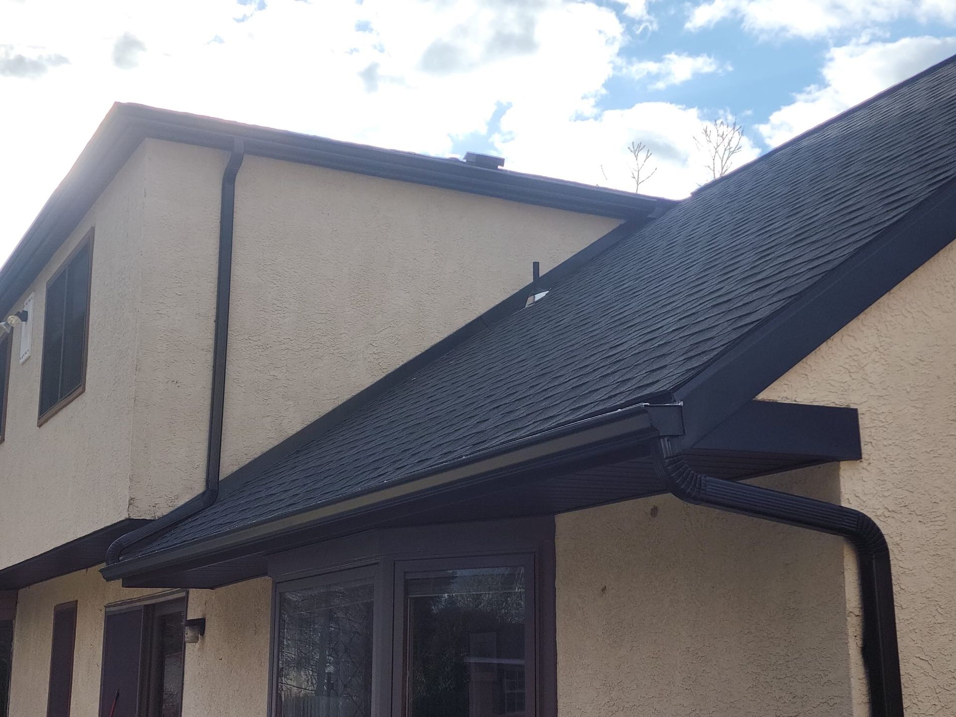 Beige house with black roof, gutters, and trim against a cloudy sky.