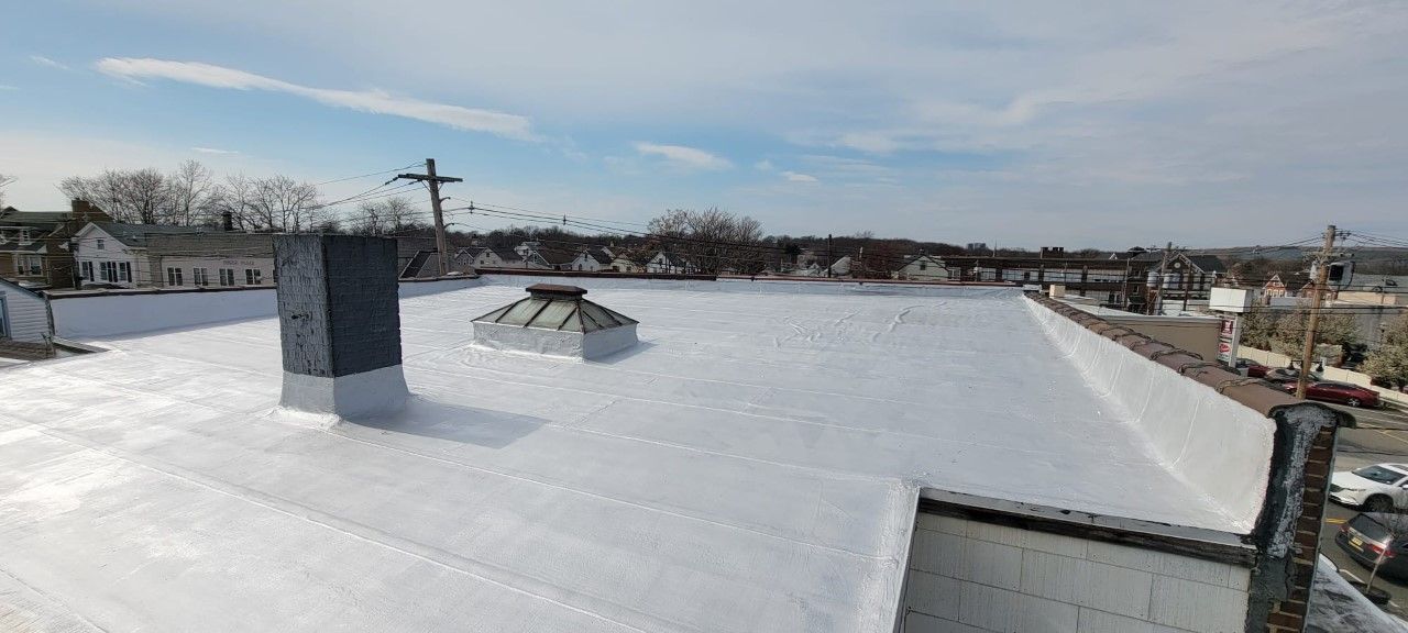 Rooftop view of a building with a white flat roof, a chimney, and a cross in the background under a blue sky.