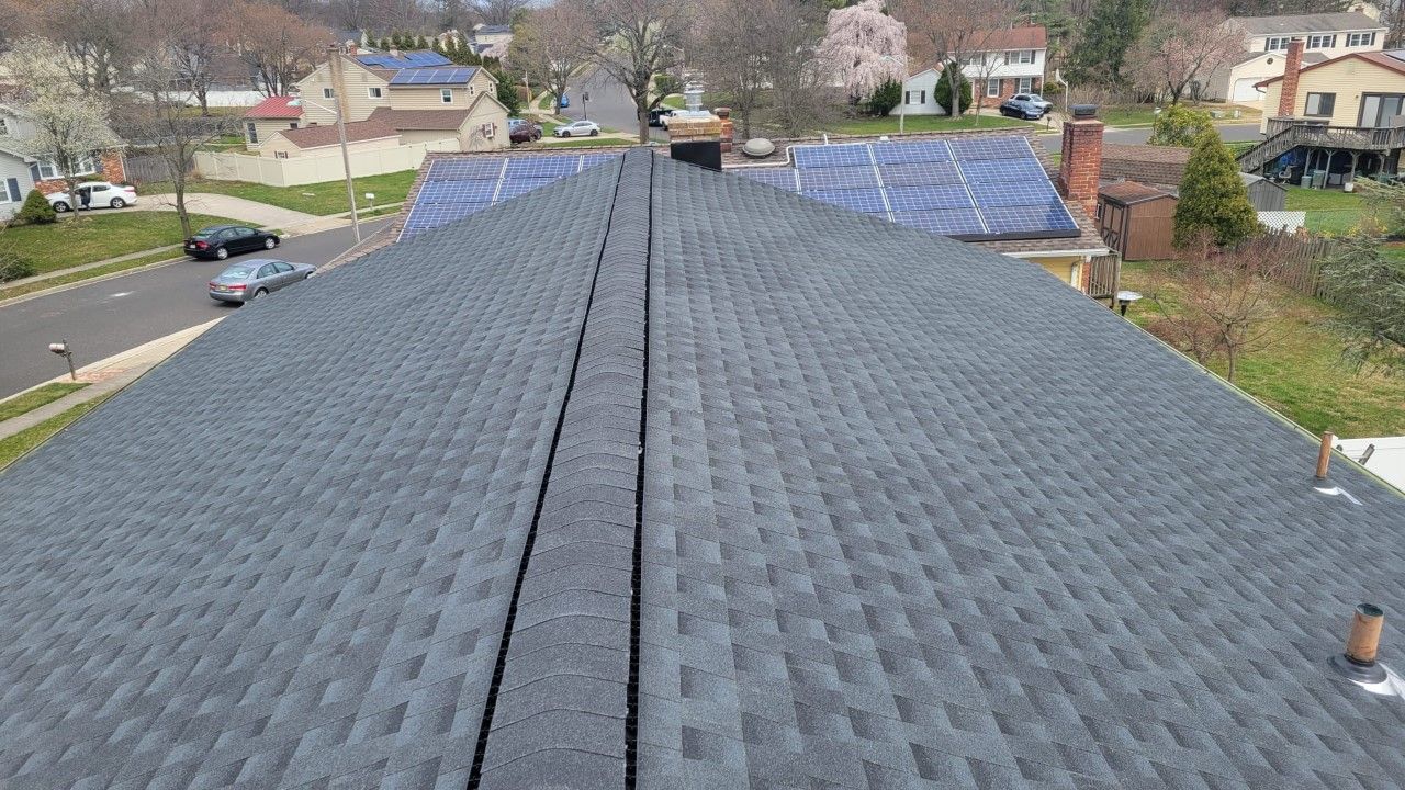 View of a gray asphalt shingle roof on a house, with a street and other houses visible.