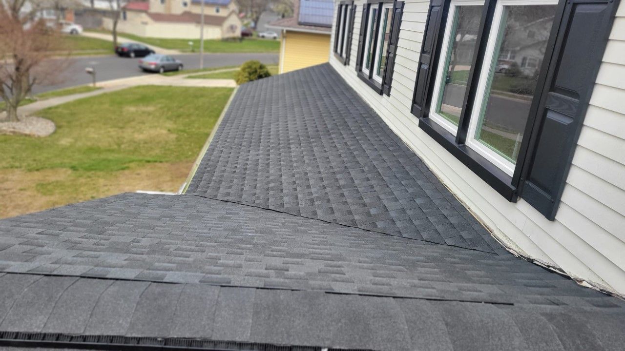 View of a gray shingled roof on a house with white siding and black shutters.
