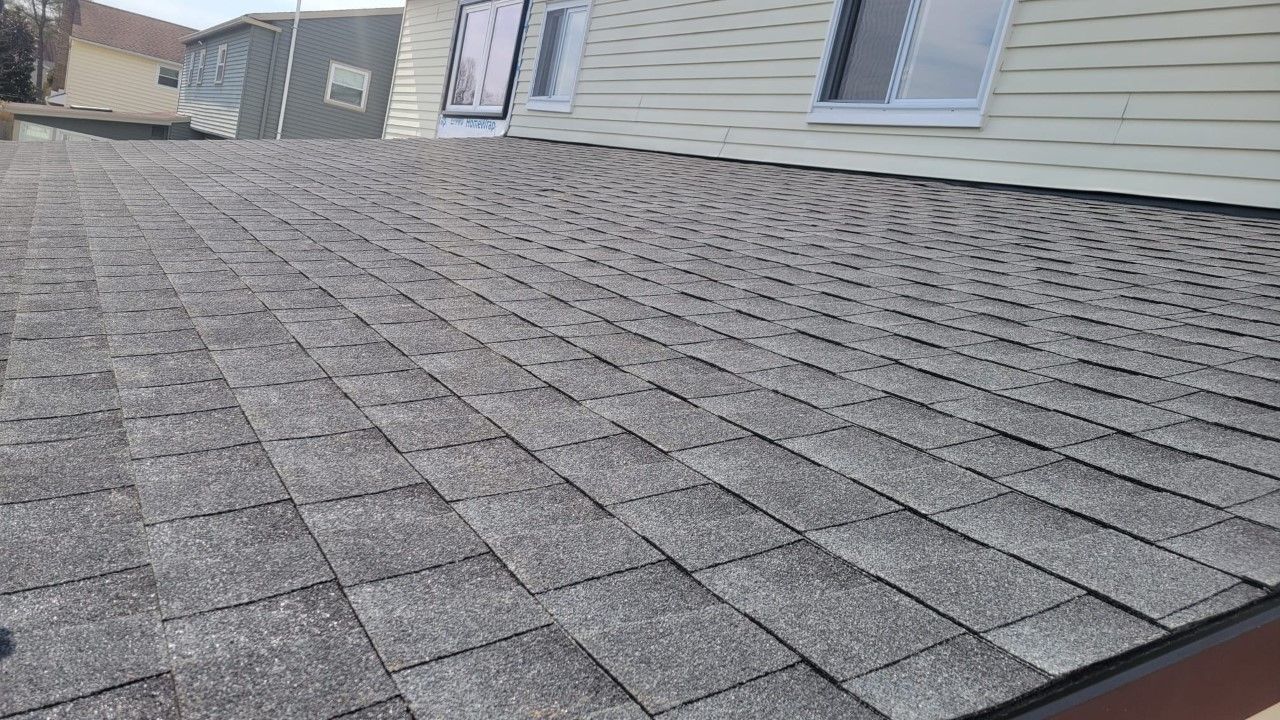 Gray asphalt shingle roof on a house, with a slight angle, sunny outdoor setting.