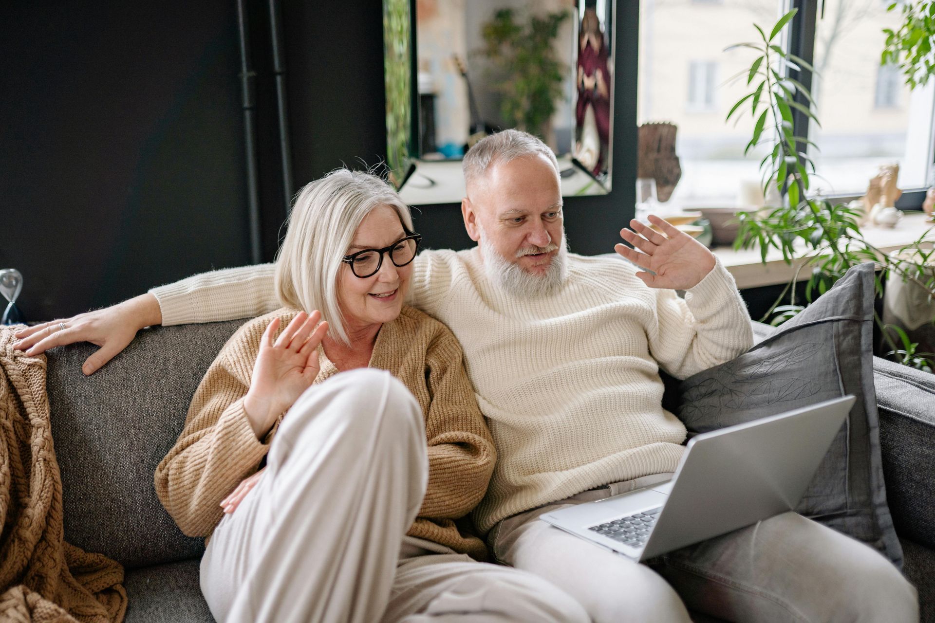 An older couple is sitting on a couch using a laptop computer.