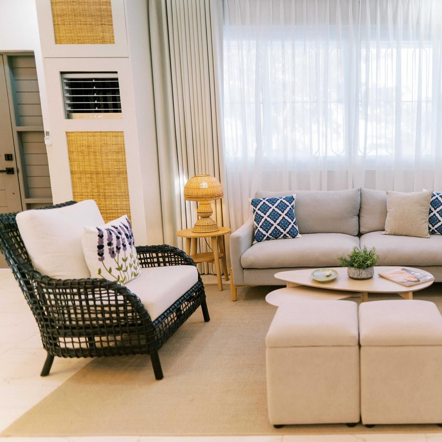 Living room with grey sofa, white curtains, and a rattan chair.