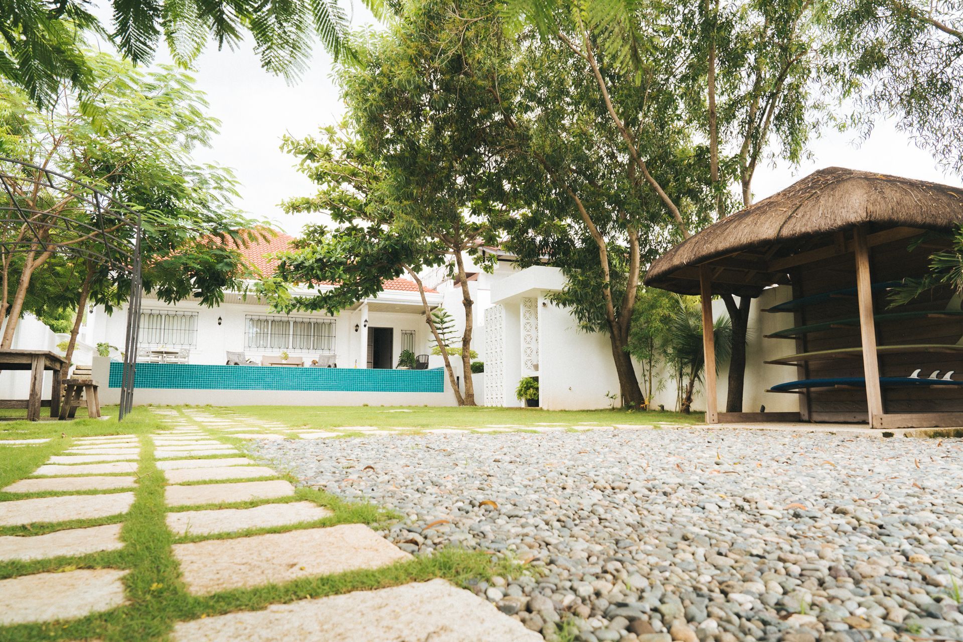 Stone path leads to white building and thatched-roof gazebo in a grassy yard.