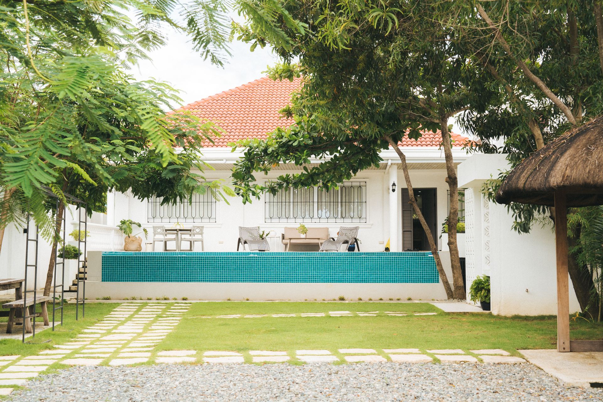 White house with a red roof and teal pool, trees surround the lawn.