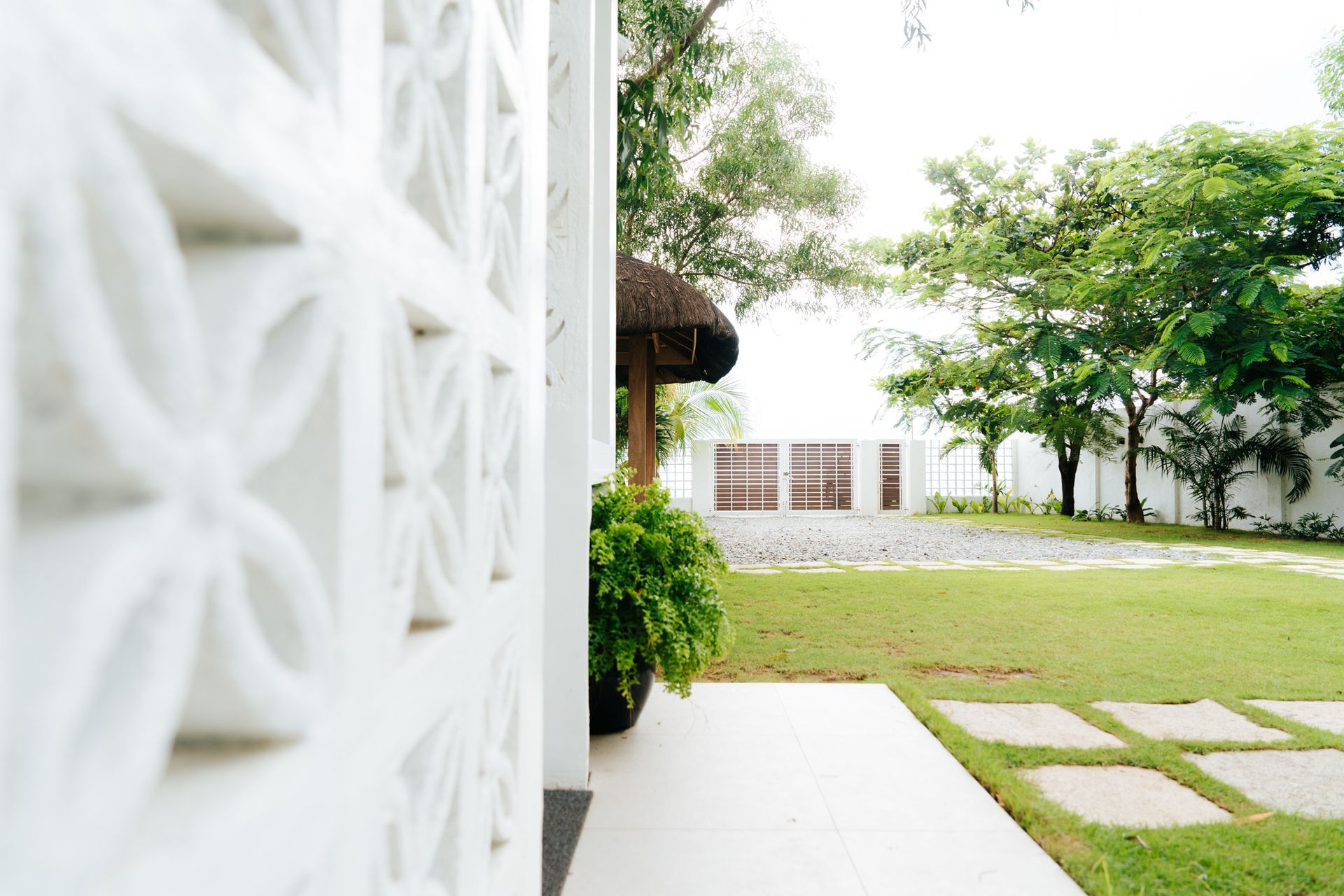White floral-patterned wall with a view of a green lawn, trees, and white buildings in the background.