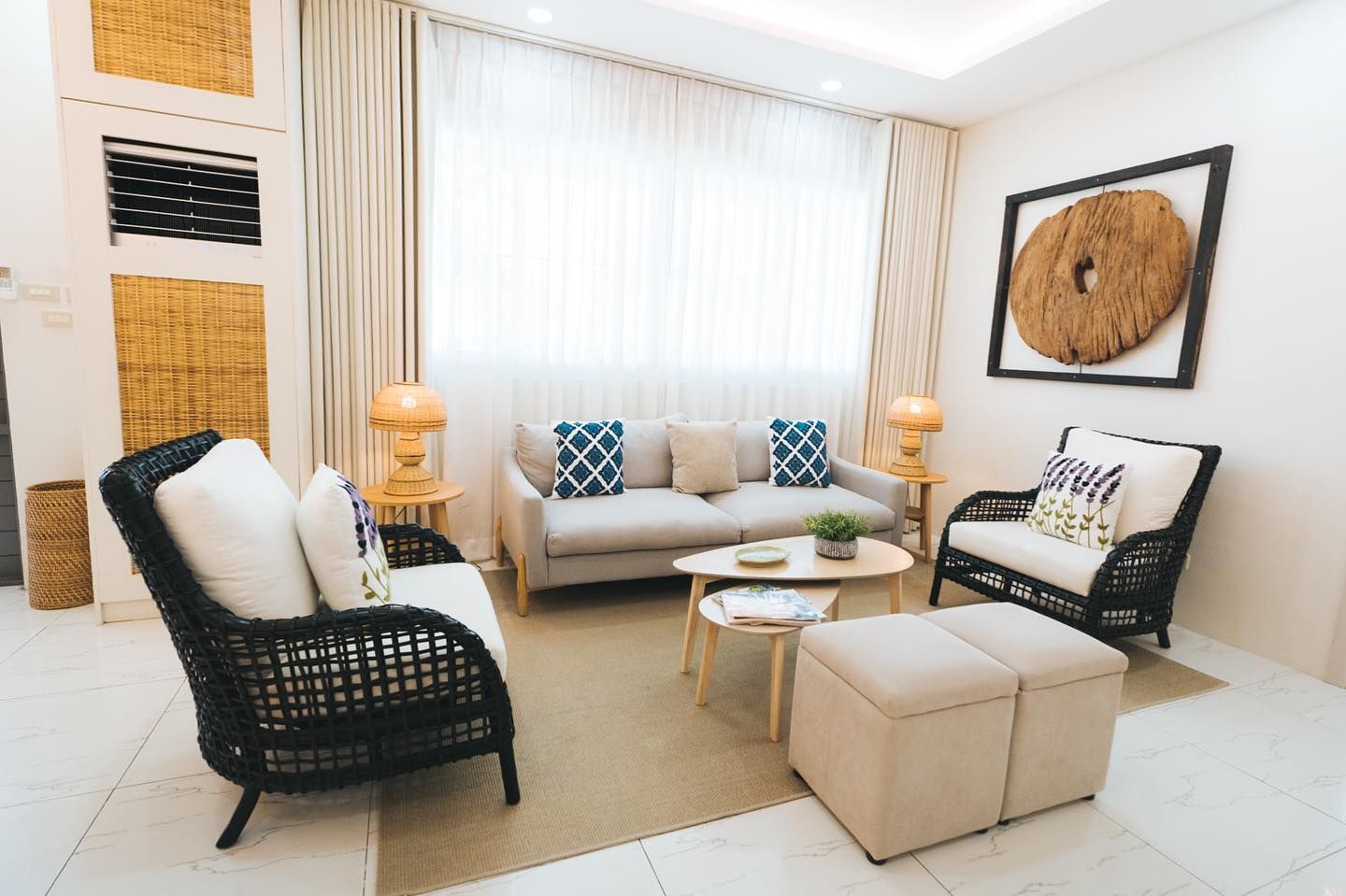 Living room with light-colored furniture, rug, and artwork. Natural light floods the space.