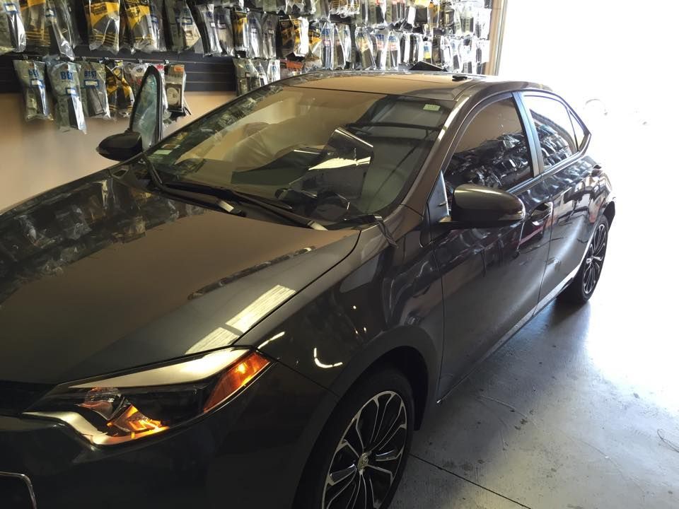 Black sedan parked in a garage with hanging tools and shelves in the background