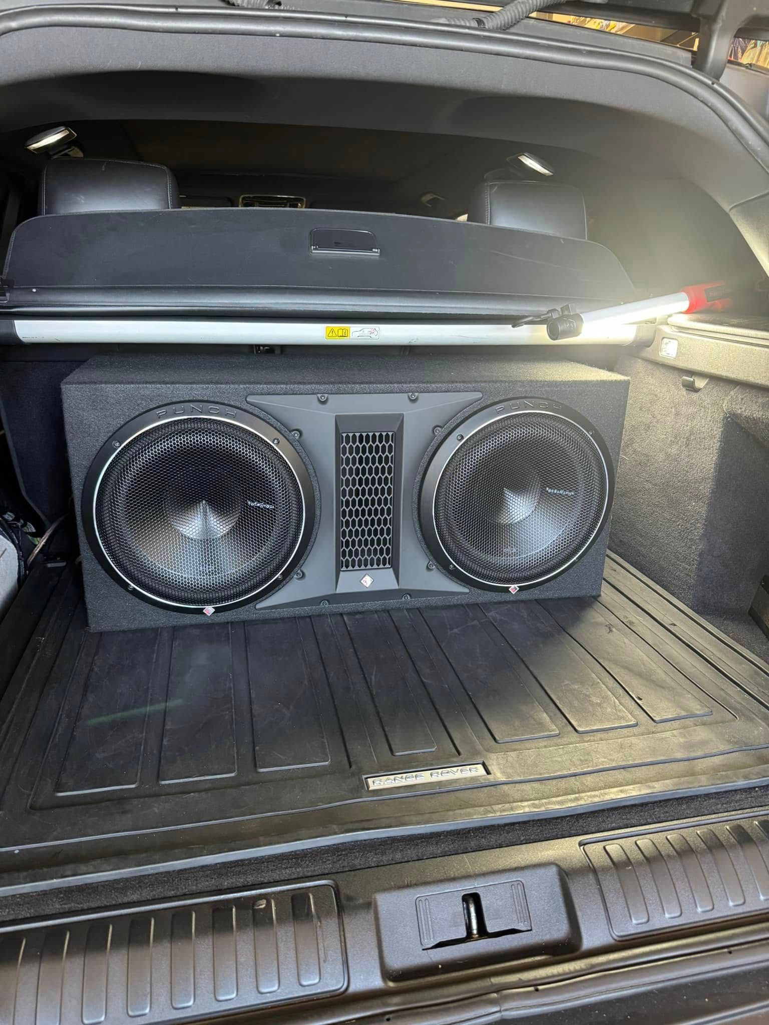 Car trunk with two large subwoofers installed behind a black cargo mat.