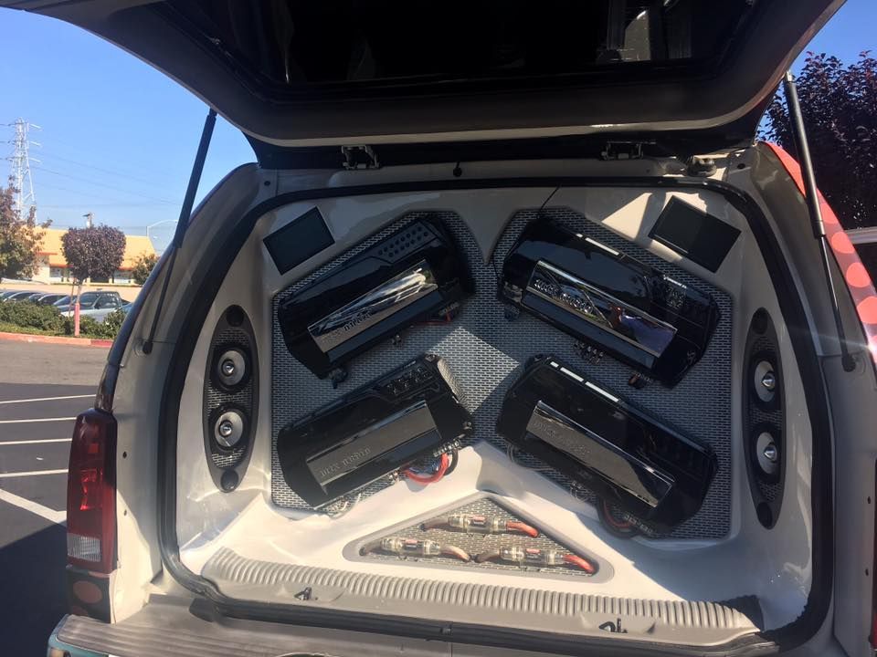 Car trunk with four black speaker boxes mounted inside a white soundproofed panel.