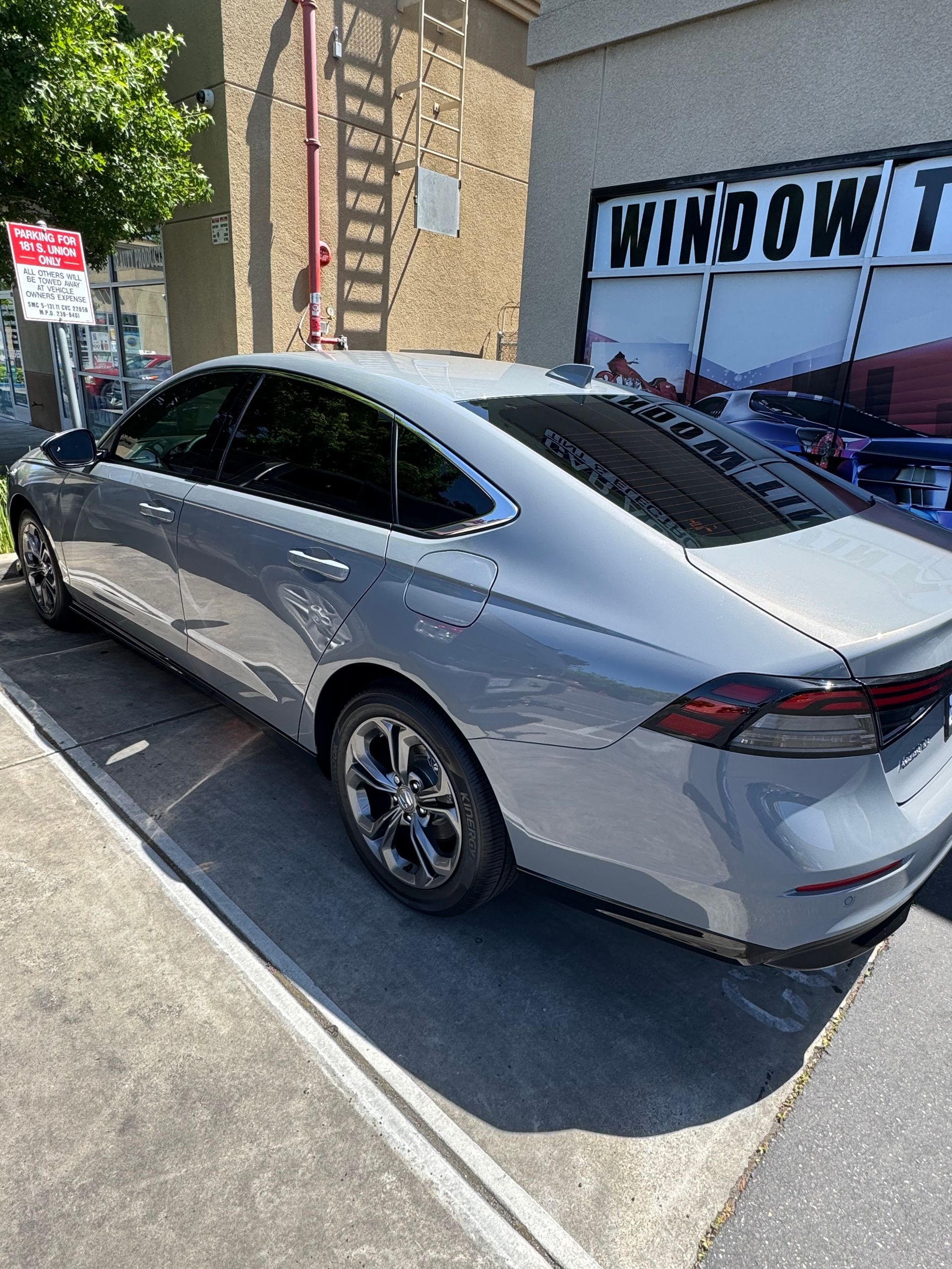 Silver sedan parked beside a building with a window tint sign in the background