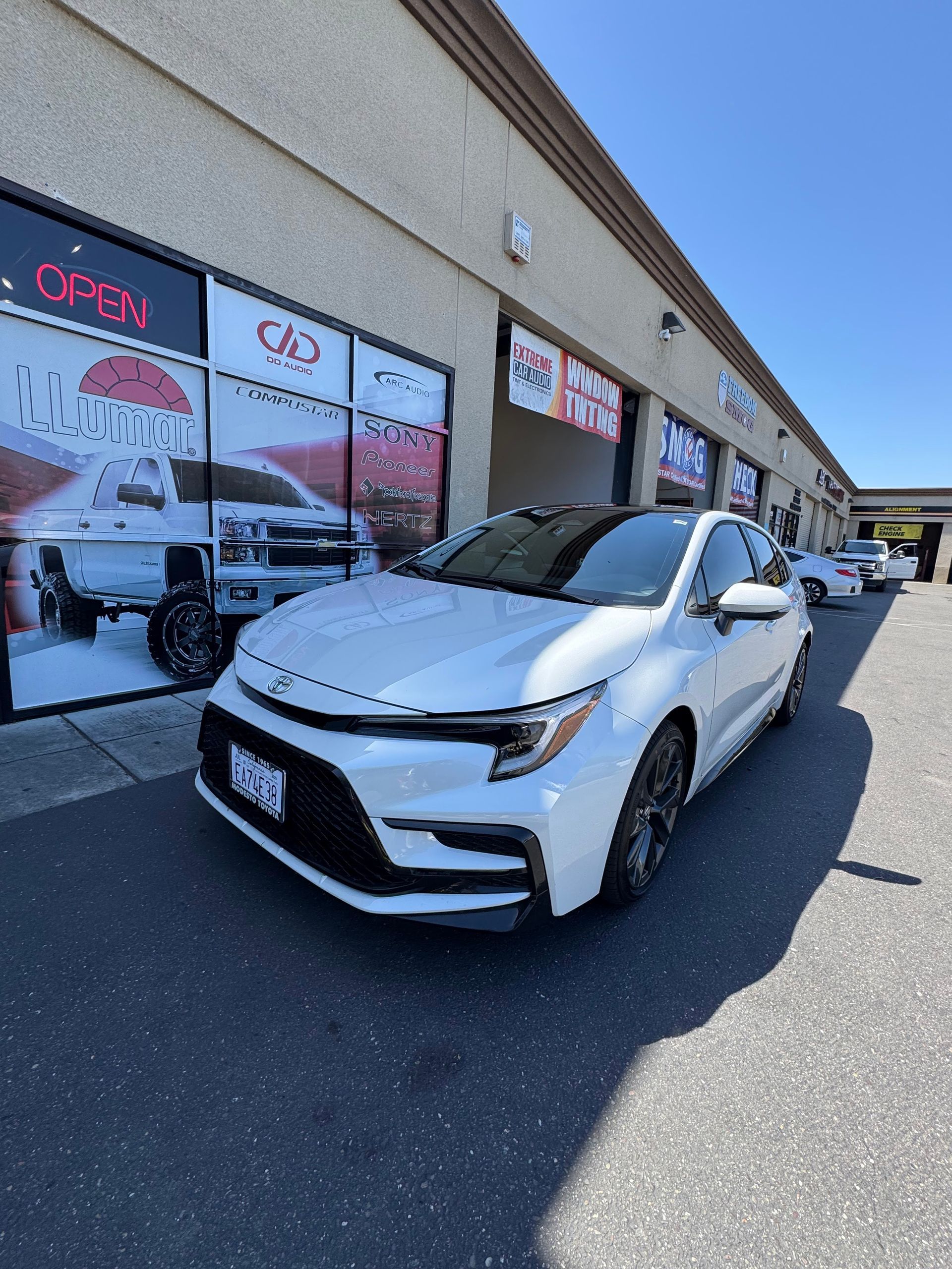 White sedan parked outside a strip mall on a sunny day