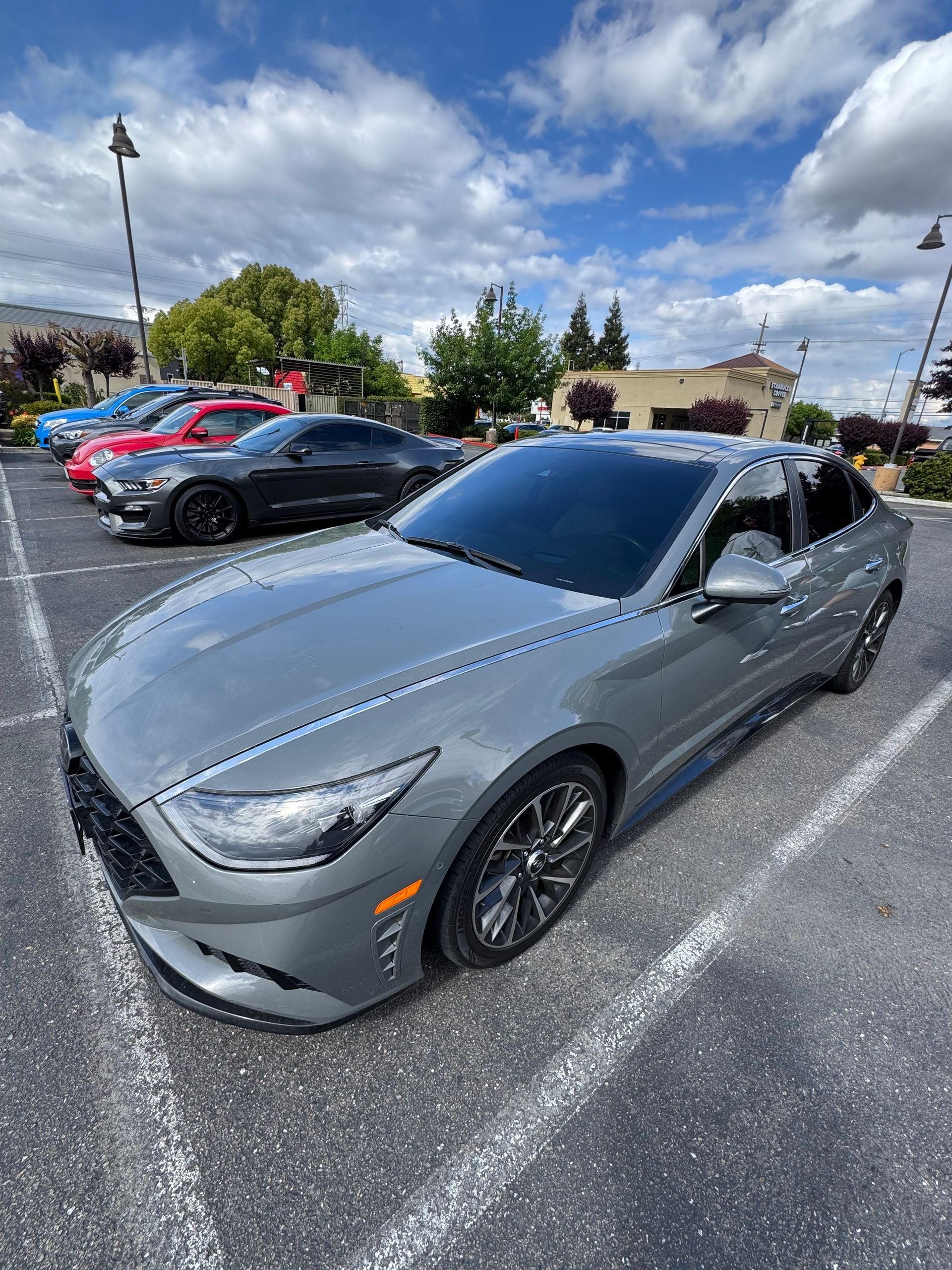 Gray convertible sports car parked in a lot under a partly cloudy sky