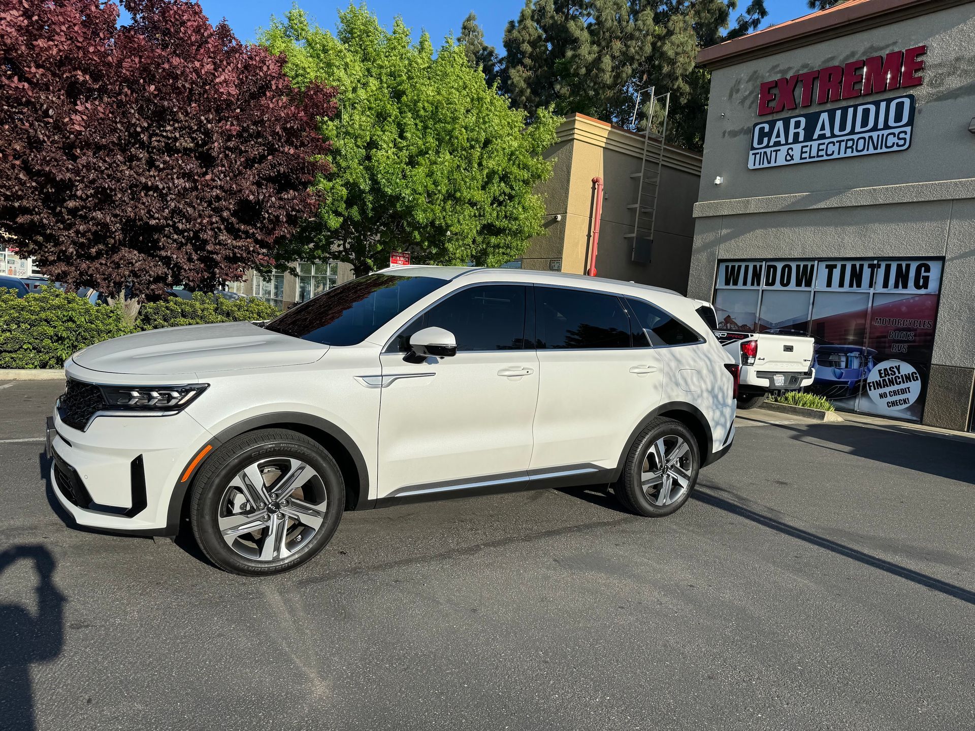 White SUV parked outside a car audio and window tinting shop on a sunny day