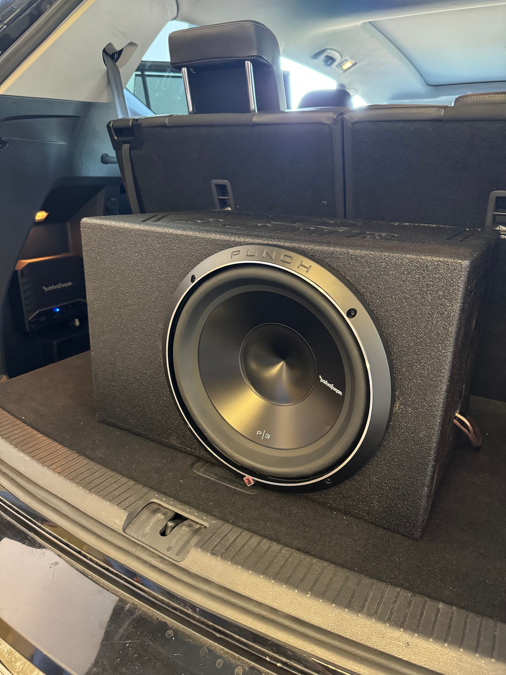 Black subwoofer speaker in a car trunk with the rear seats folded down.