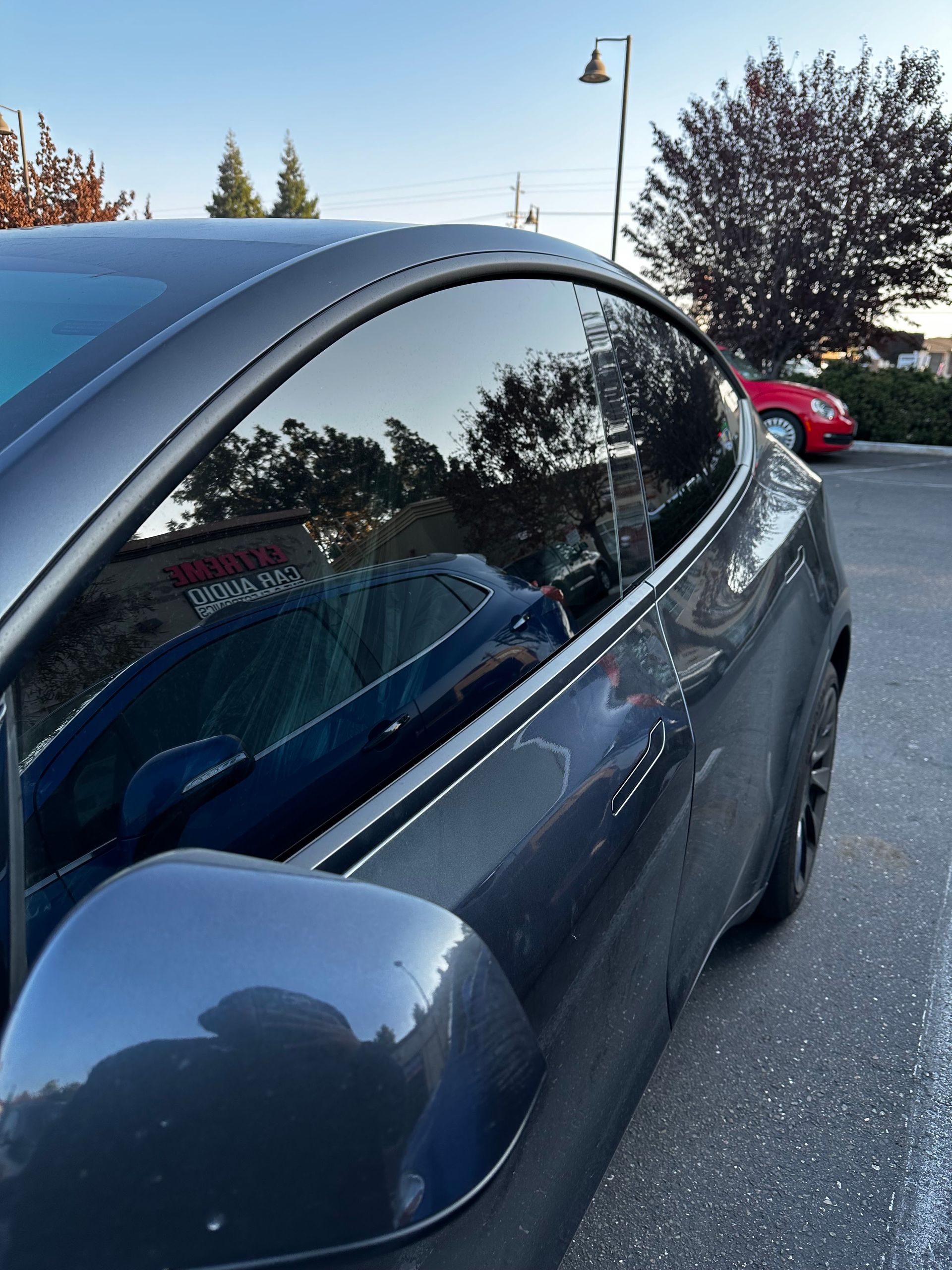 Blue parked car with side mirror and tinted windows on a snowy street, red car in the background