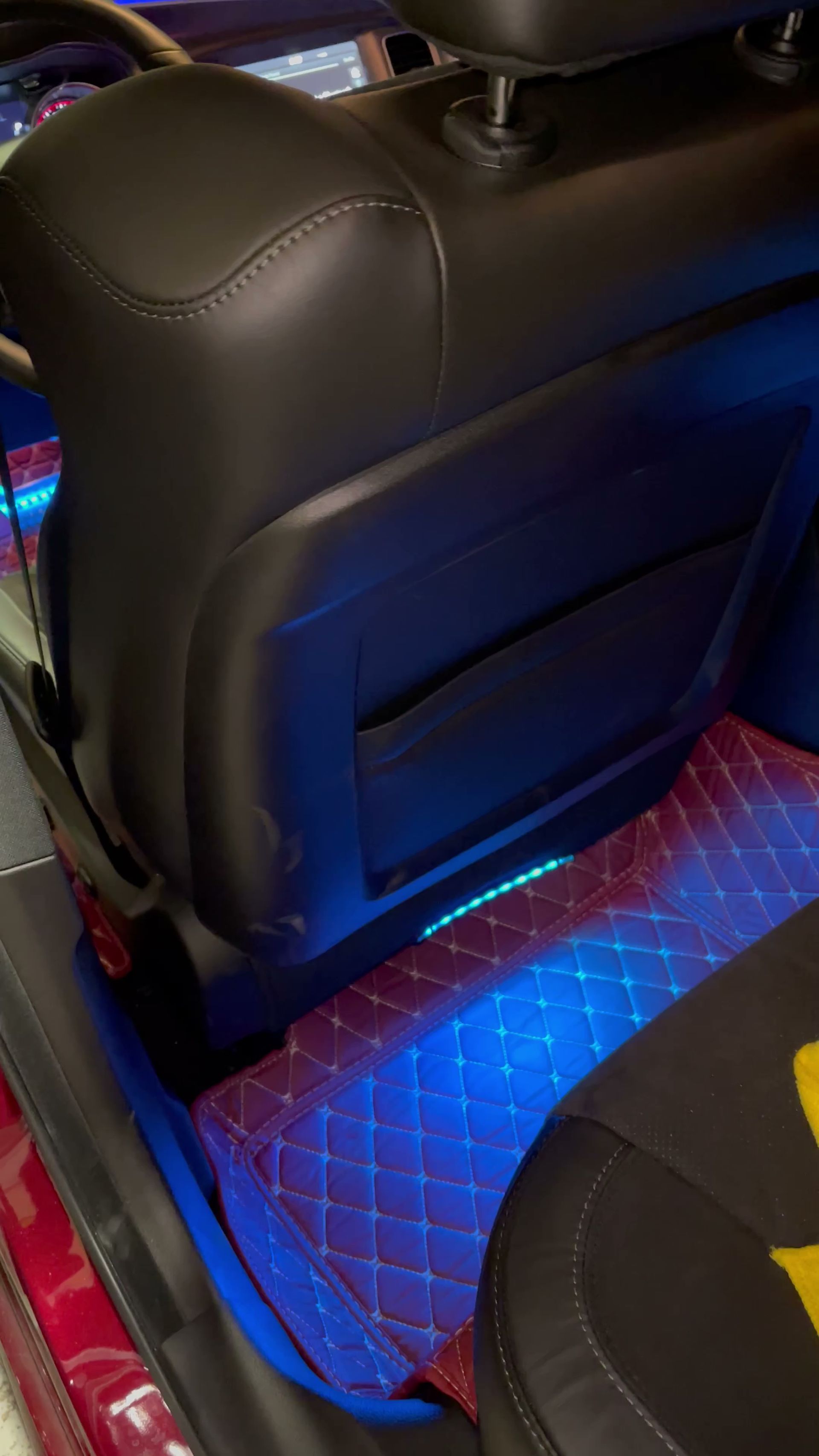 Blue LED-lit footwell under a black leather car seat with diamond-quilted floor mat
