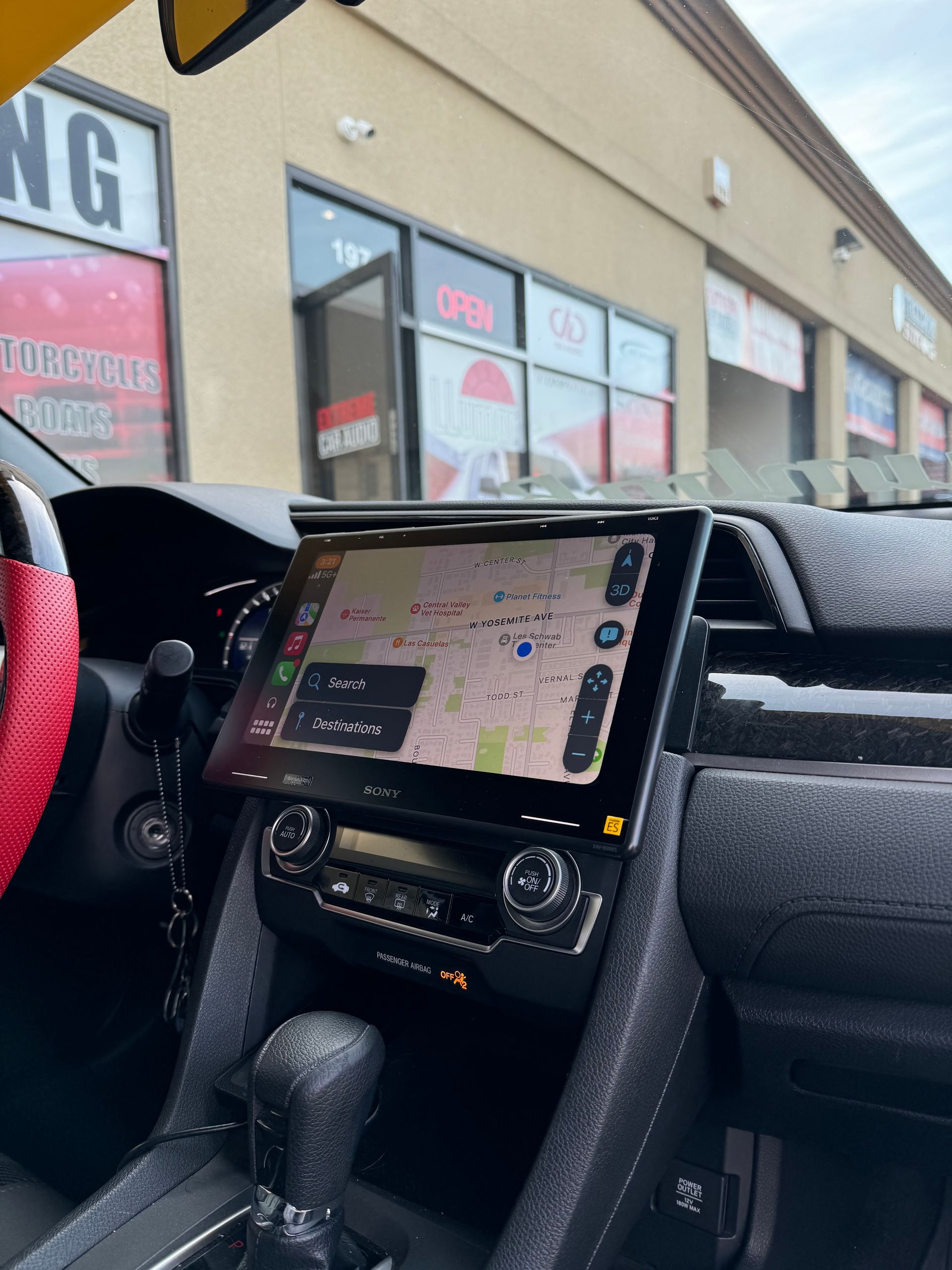 Car dashboard with a navigation screen mounted, parked outside a store.