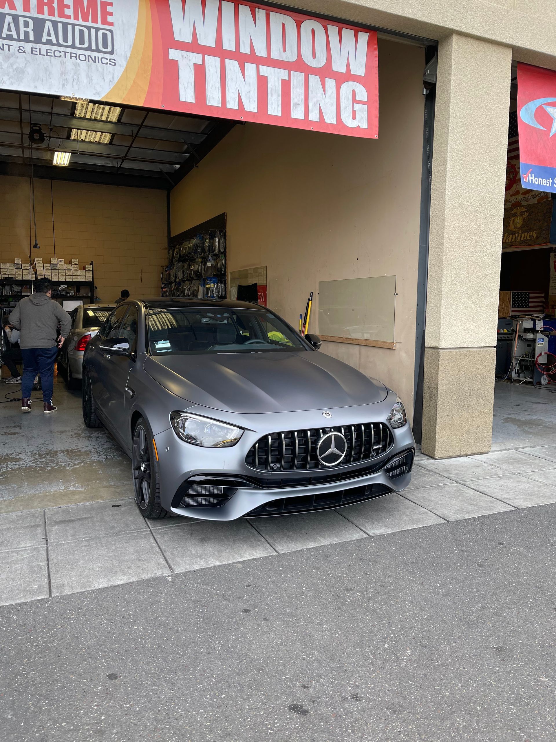 Gray Mercedes parked in a window tinting shop entrance with workers inside