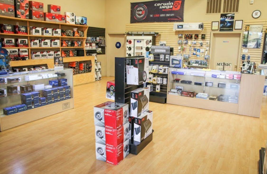 Electronics store interior with shelves of gadgets, boxed items, and display counters on a wood floor.