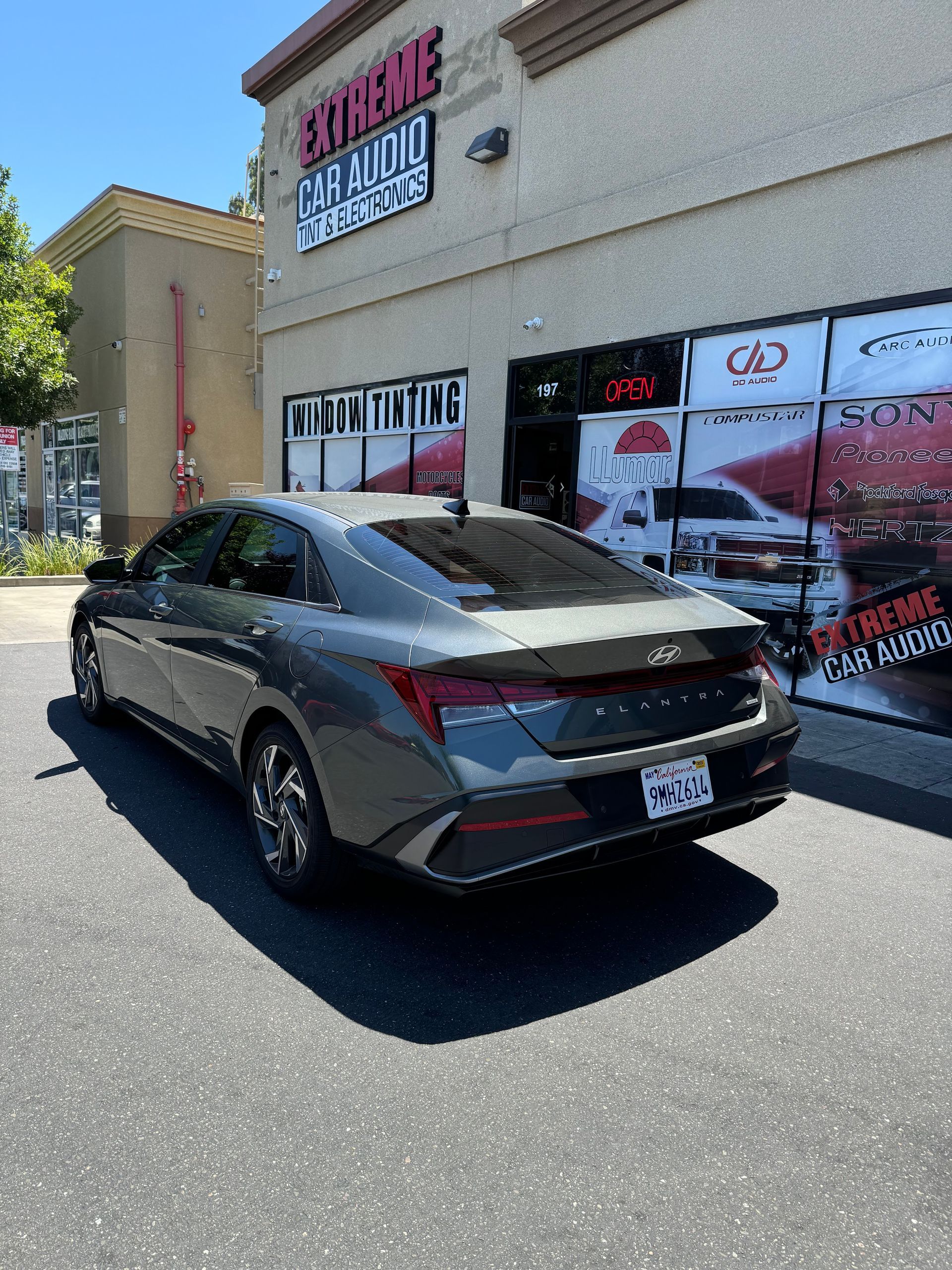 Dark gray sedan parked outside a tint shop with storefront signage and parked cars nearby