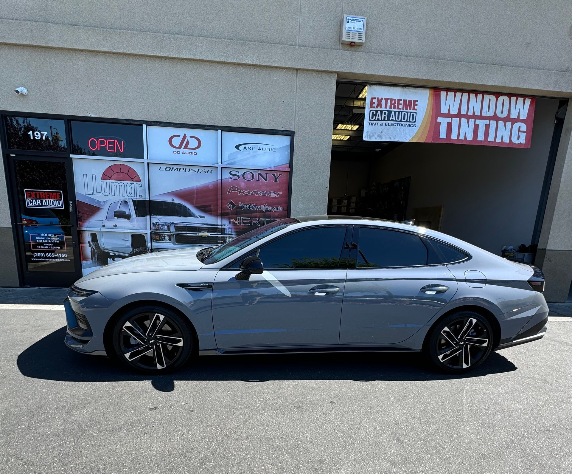Silver sedan parked outside a window tinting shop in bright sunlight.