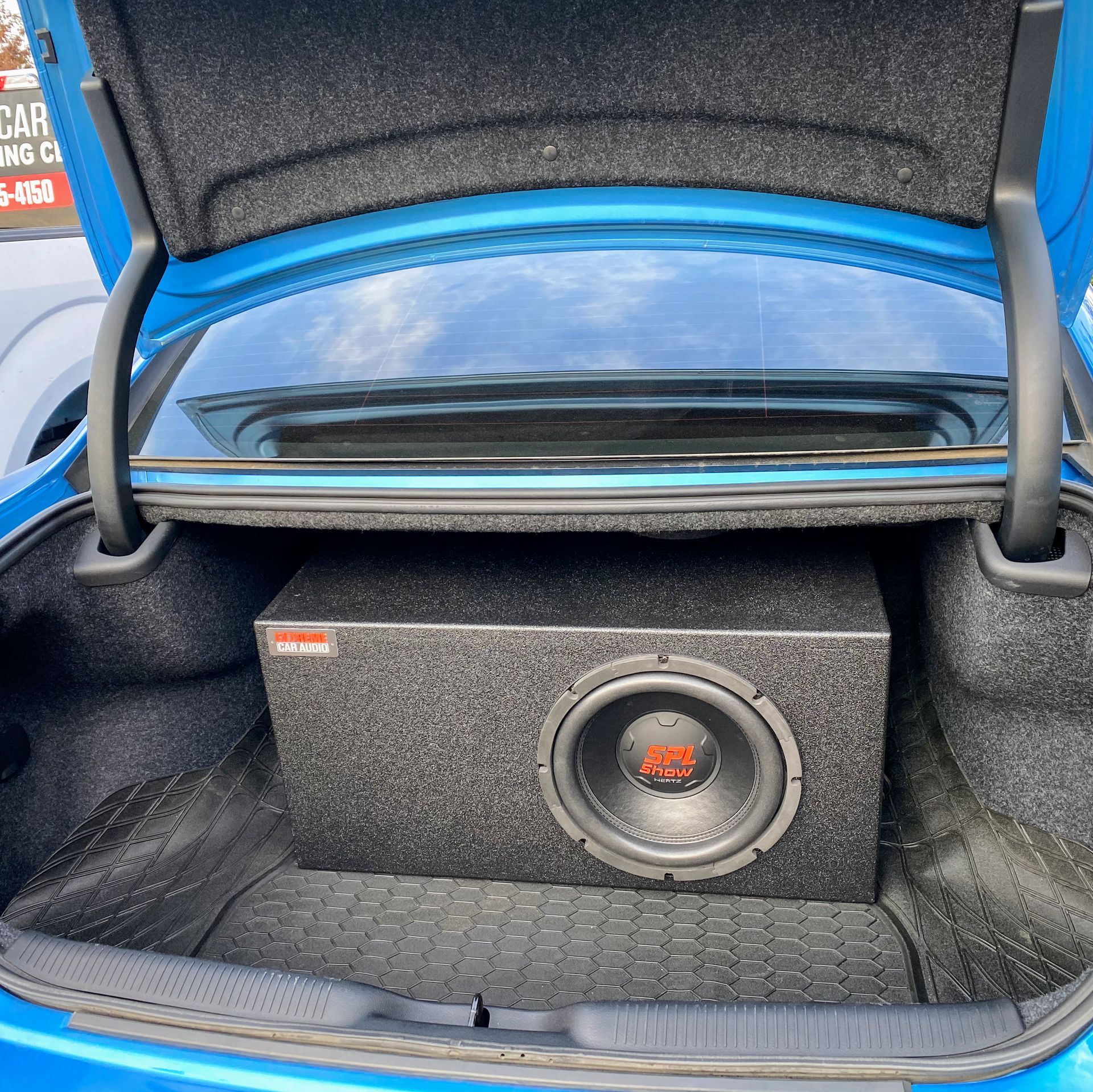 Car trunk with a large black subwoofer box and blue trim around the opening