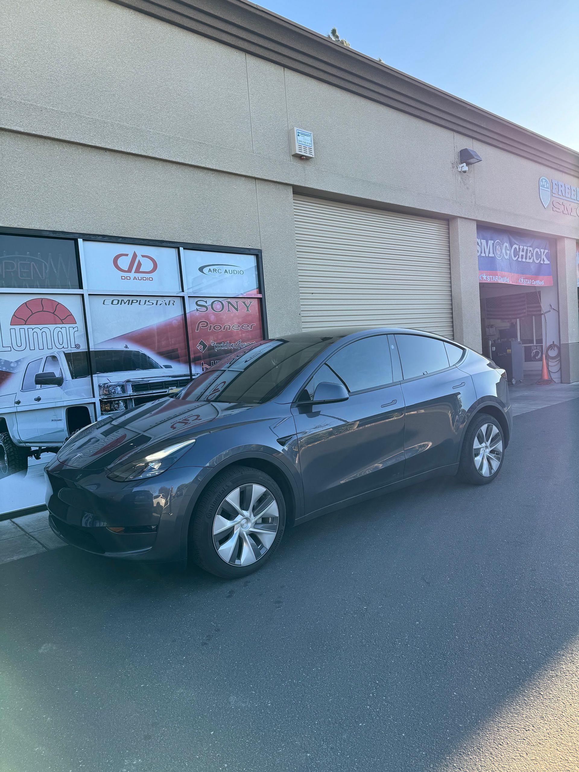 Black Tesla parked outside a storefront with sun glare on the right side of the image.