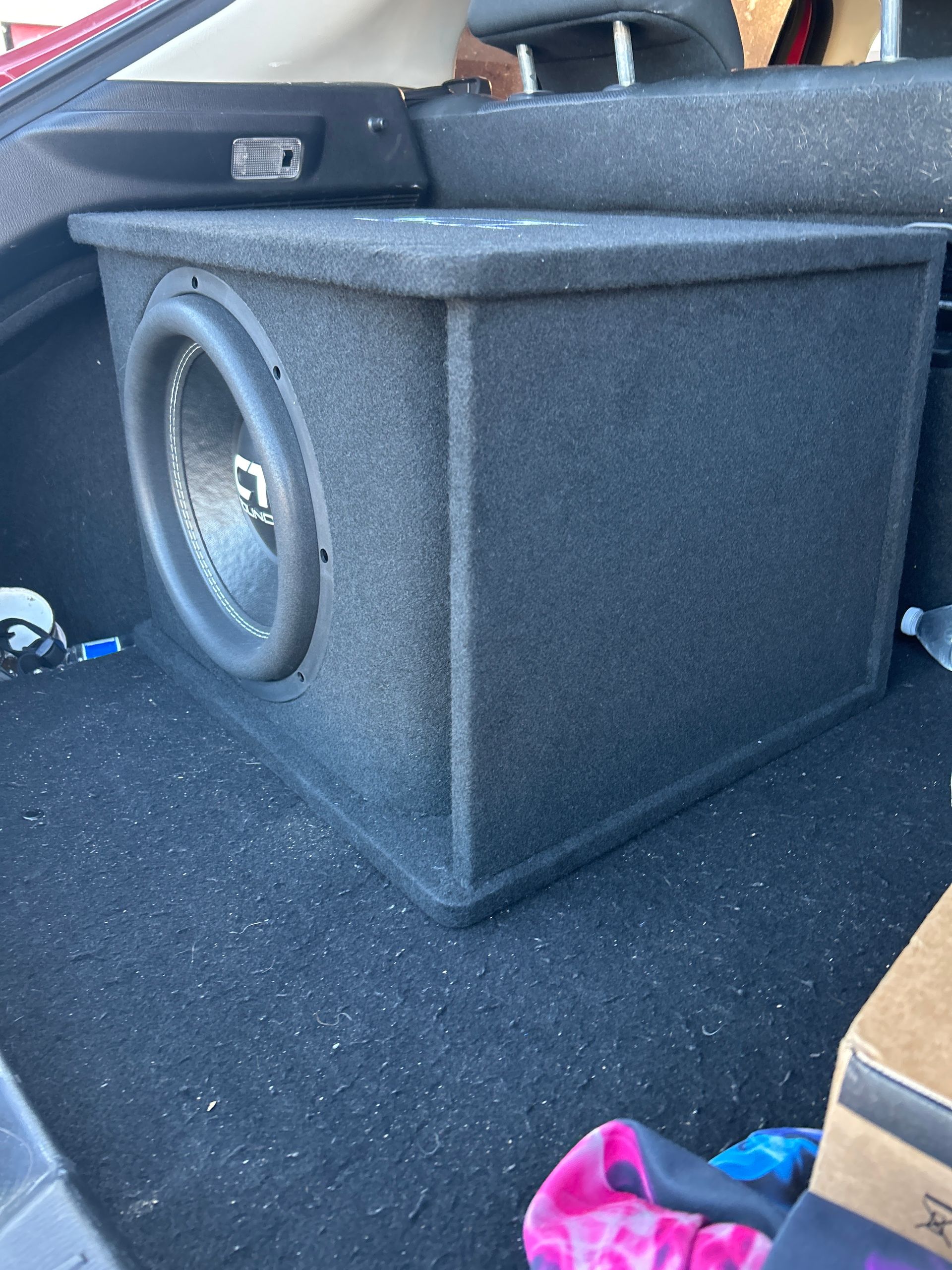 Black subwoofer box in a car trunk on a carpeted floor.