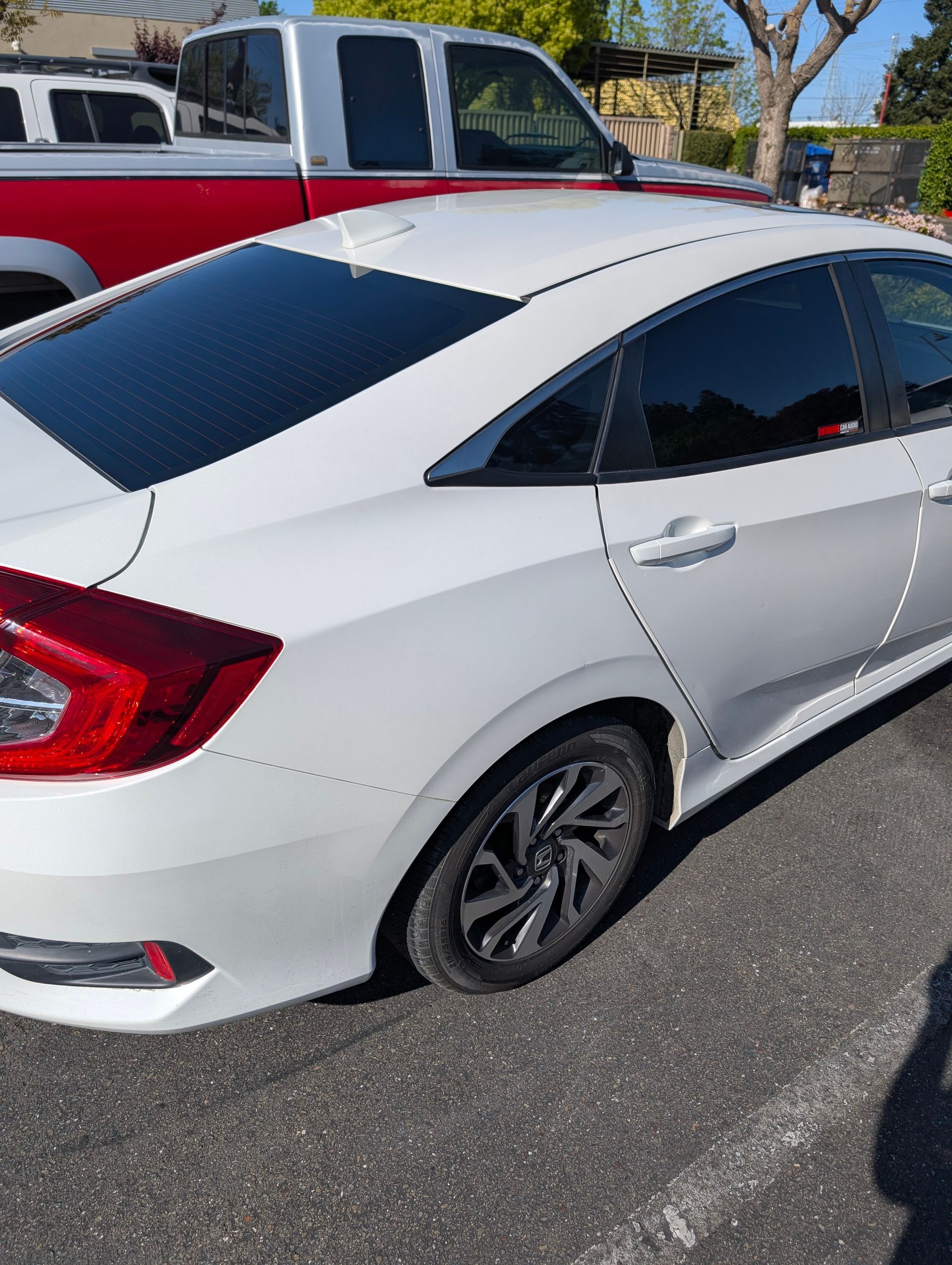 White sedan with tinted windows parked outdoors beside a red-and-white pickup truck.