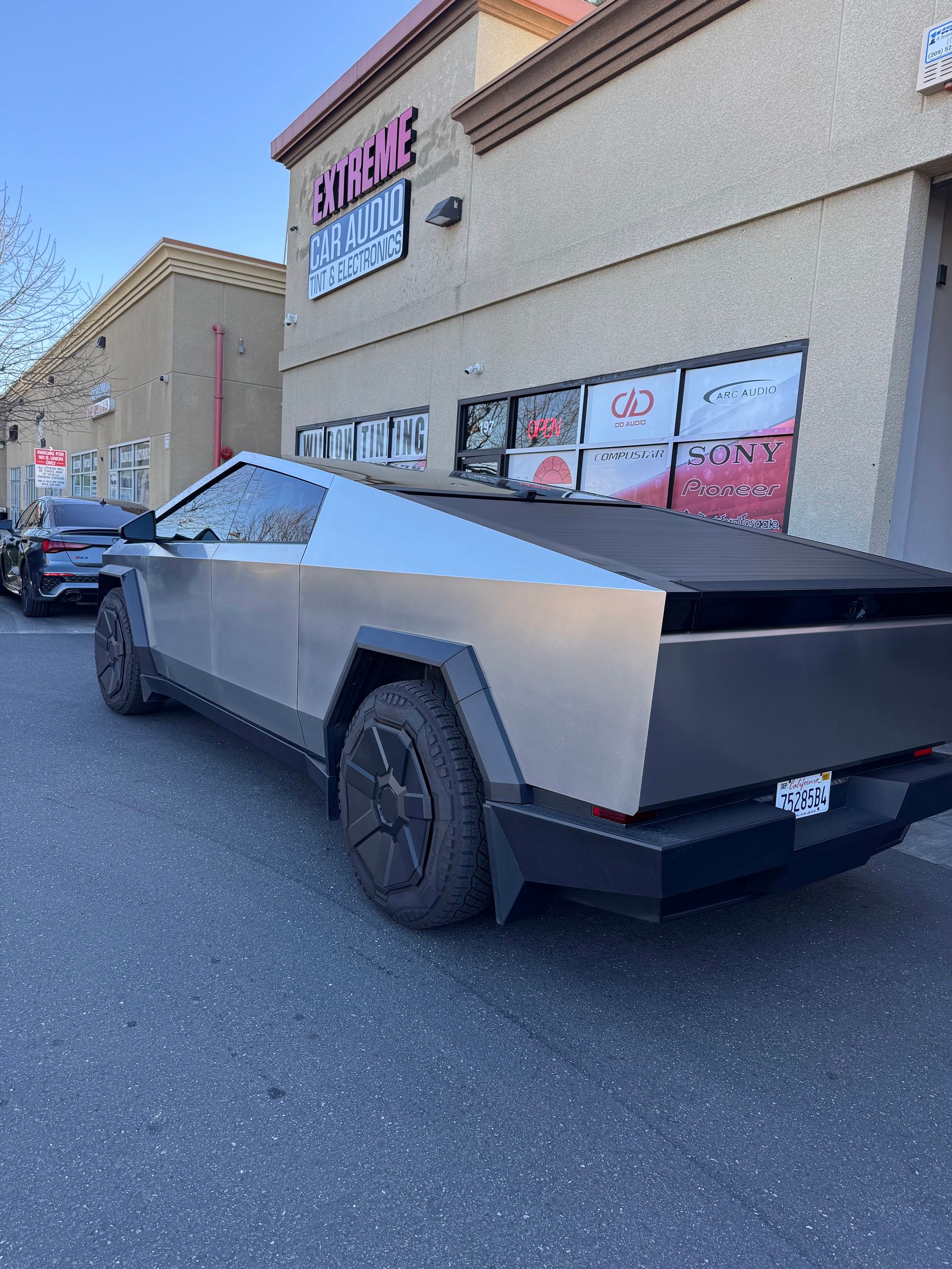 Tesla Cybertruck parked beside a beige building with storefront windows and a snowy bed cover.