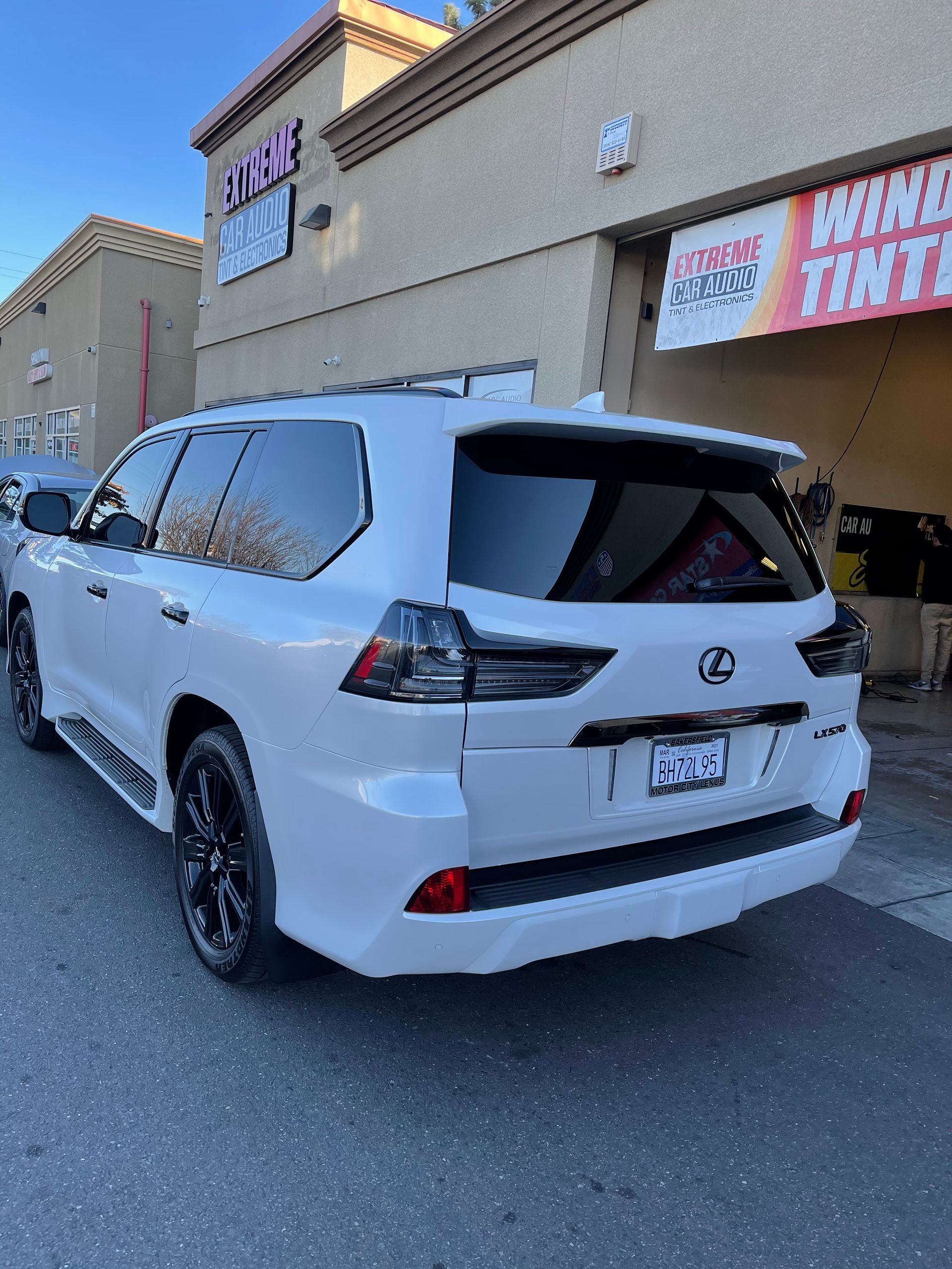 White SUV parked outside a shop with a large open rear window and tinted glass, under a storefront awning.
