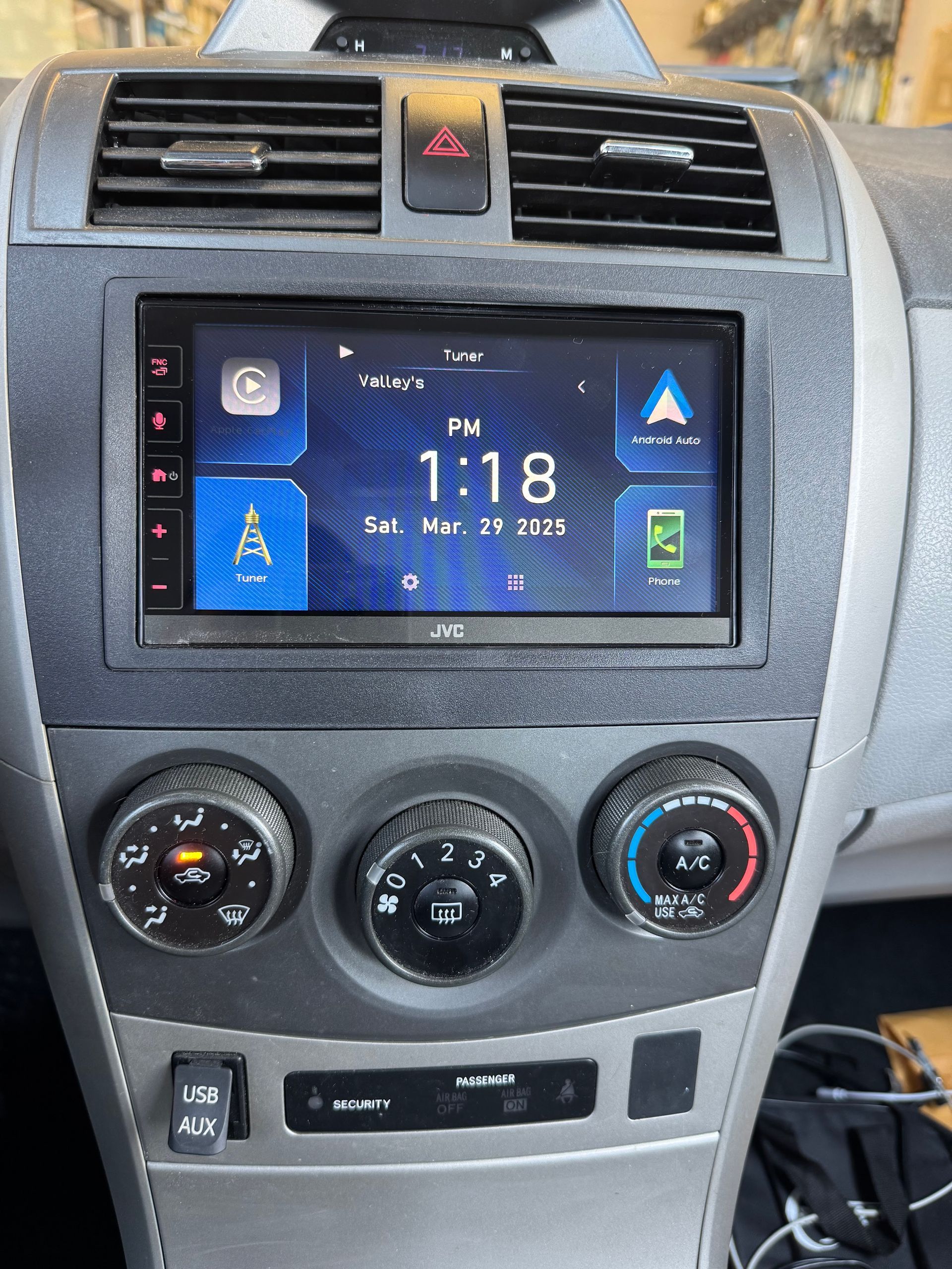 Car dashboard center console with touchscreen display, air vents, climate knobs, and buttons.