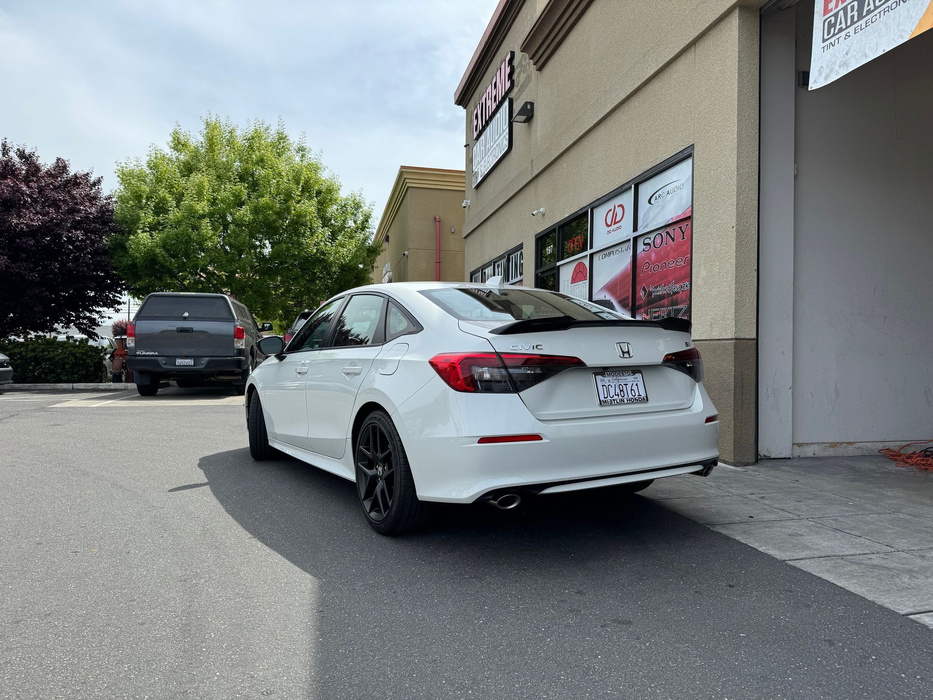 White sedan parked beside a beige storefront on a sunny street.