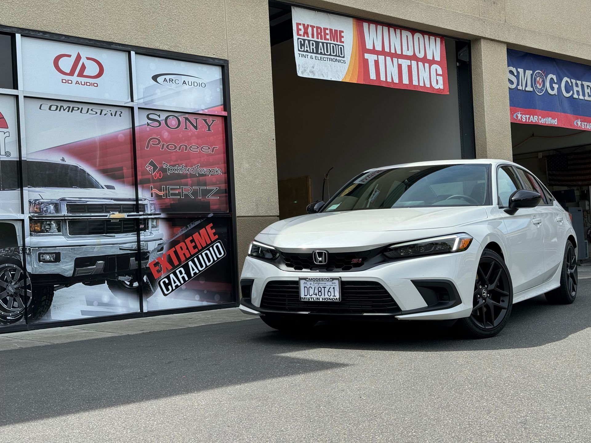White Honda sedan parked outside an auto window tinting shop with promotional signs in the windows