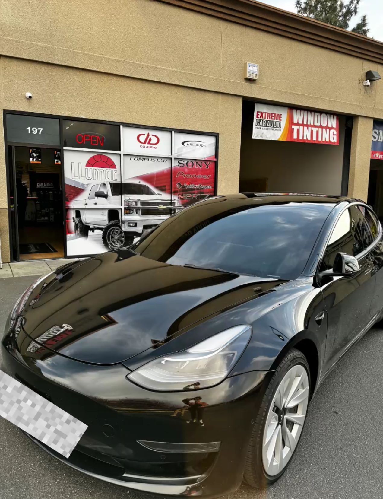 Black sports sedan parked outside a car shop with a timing sign.