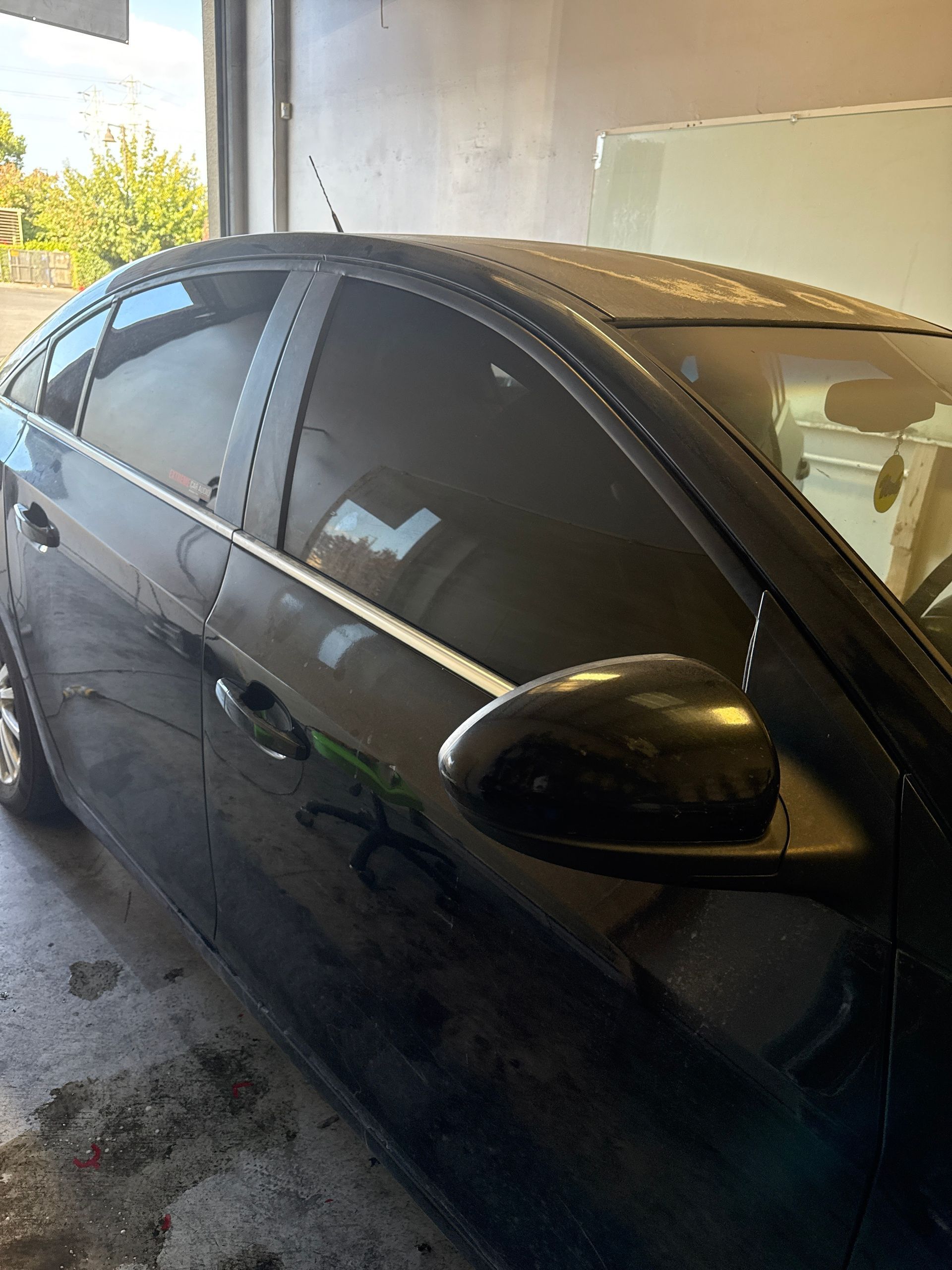 Black sedan parked in a garage, side view with tinted windows and wet floor.