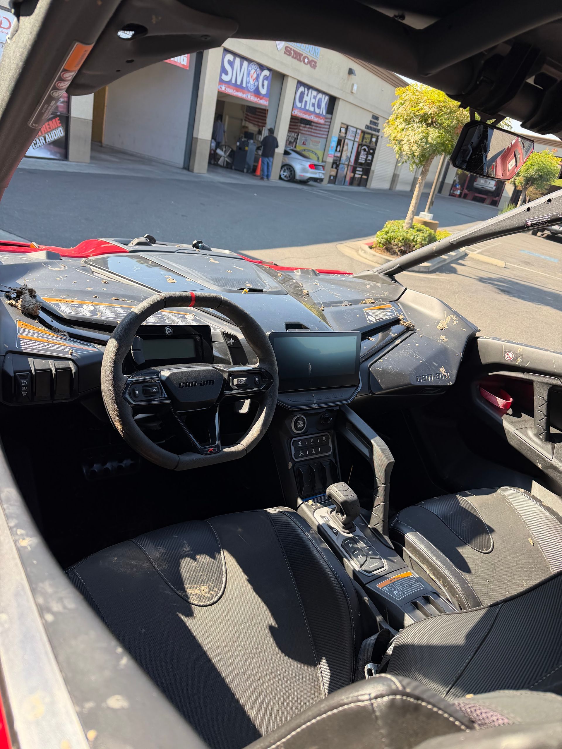 Inside a car with shattered windshield, steering wheel visible, debris scattered across the dashboard and seats.