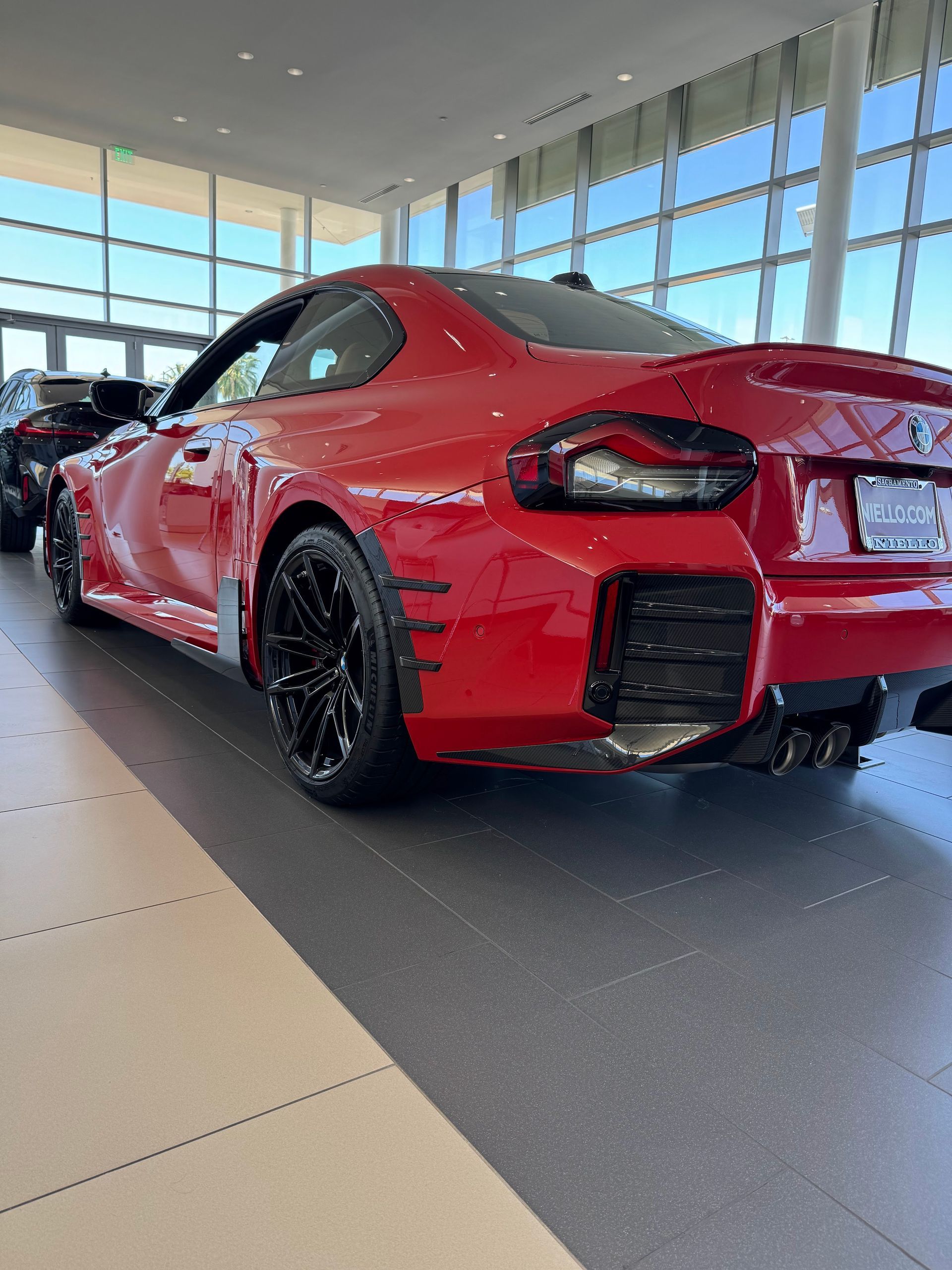 Red sports car in a bright showroom, viewed from the rear side.