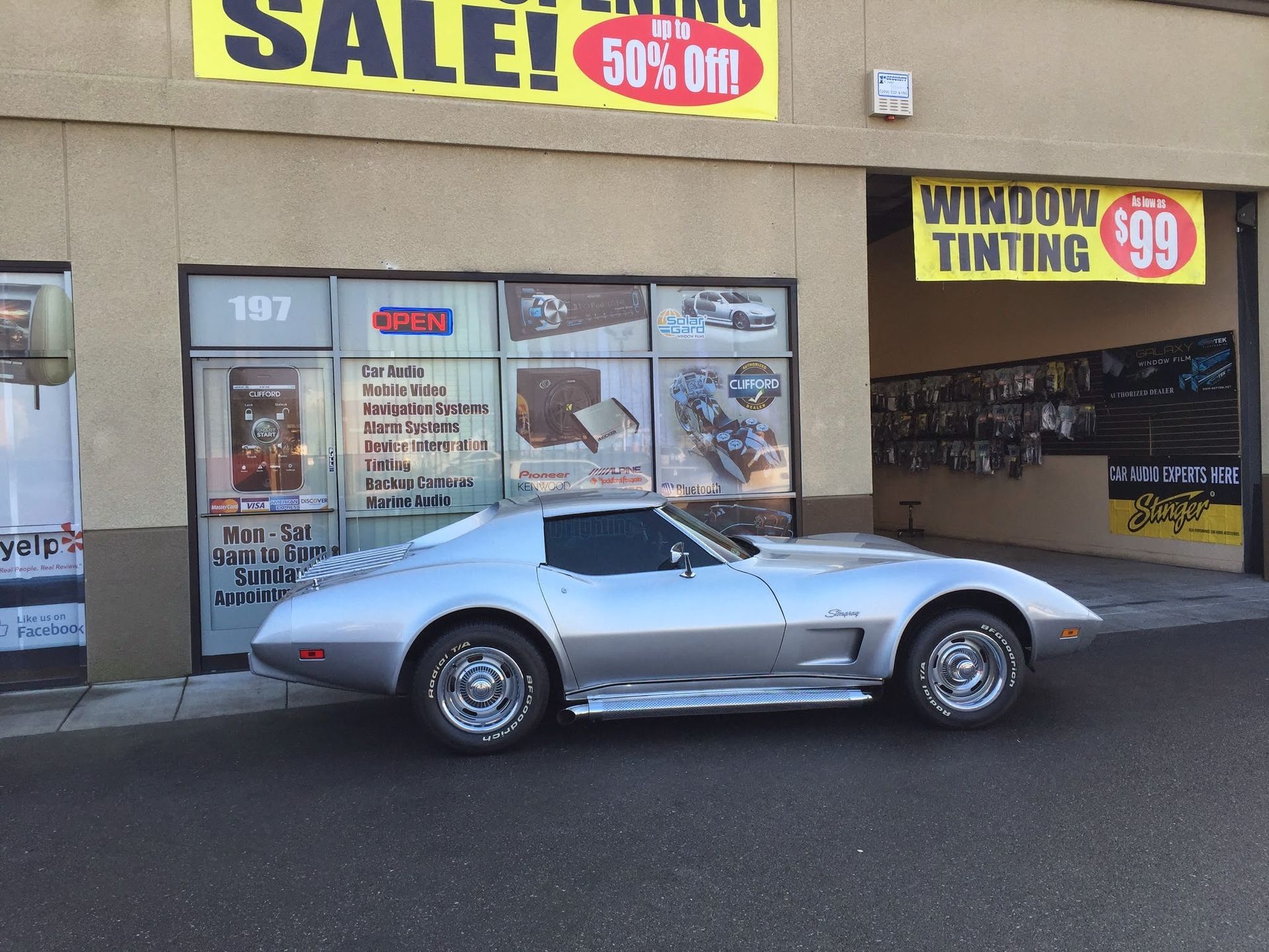 Silver sports car parked outside a storefront with sale signs in the window