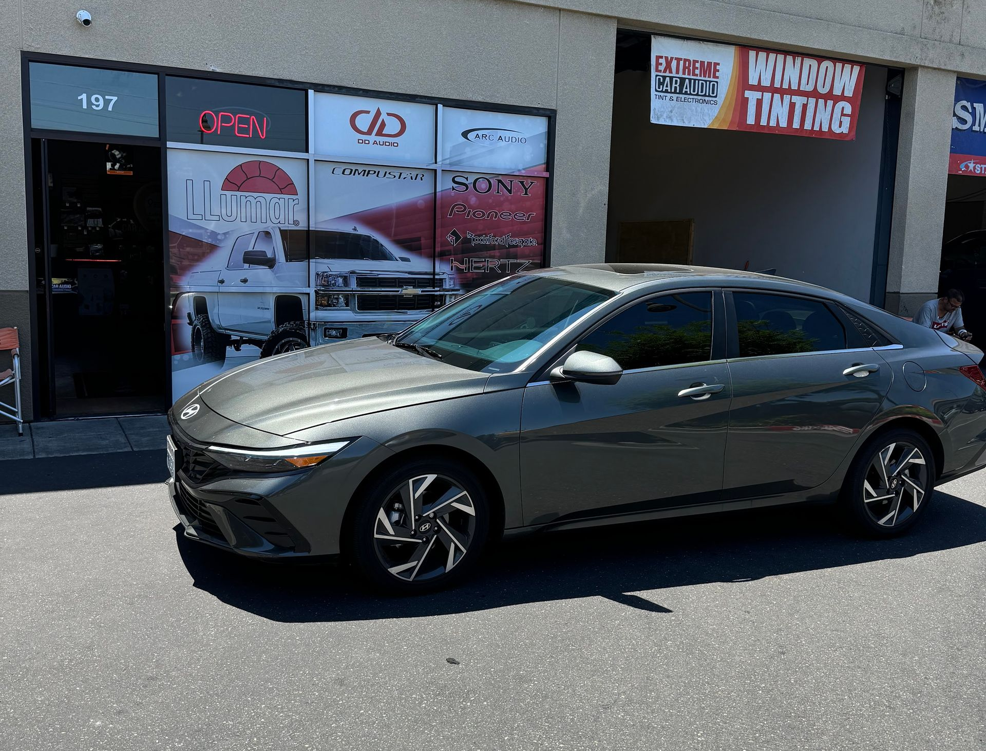 Gray sedan parked outside a window-tinting shop in bright sunlight