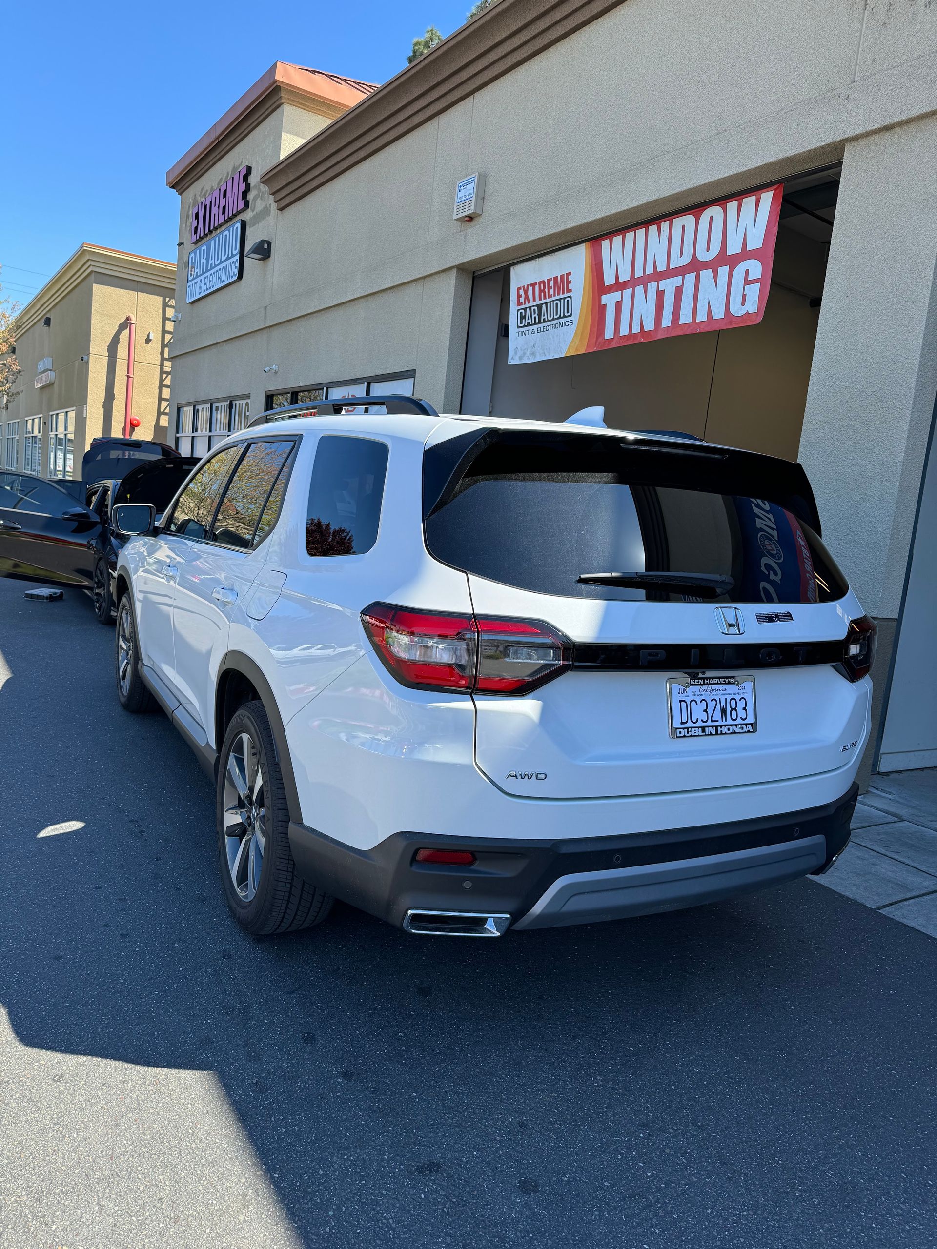 White SUV parked outside a building with a “Window Tinting” sign.