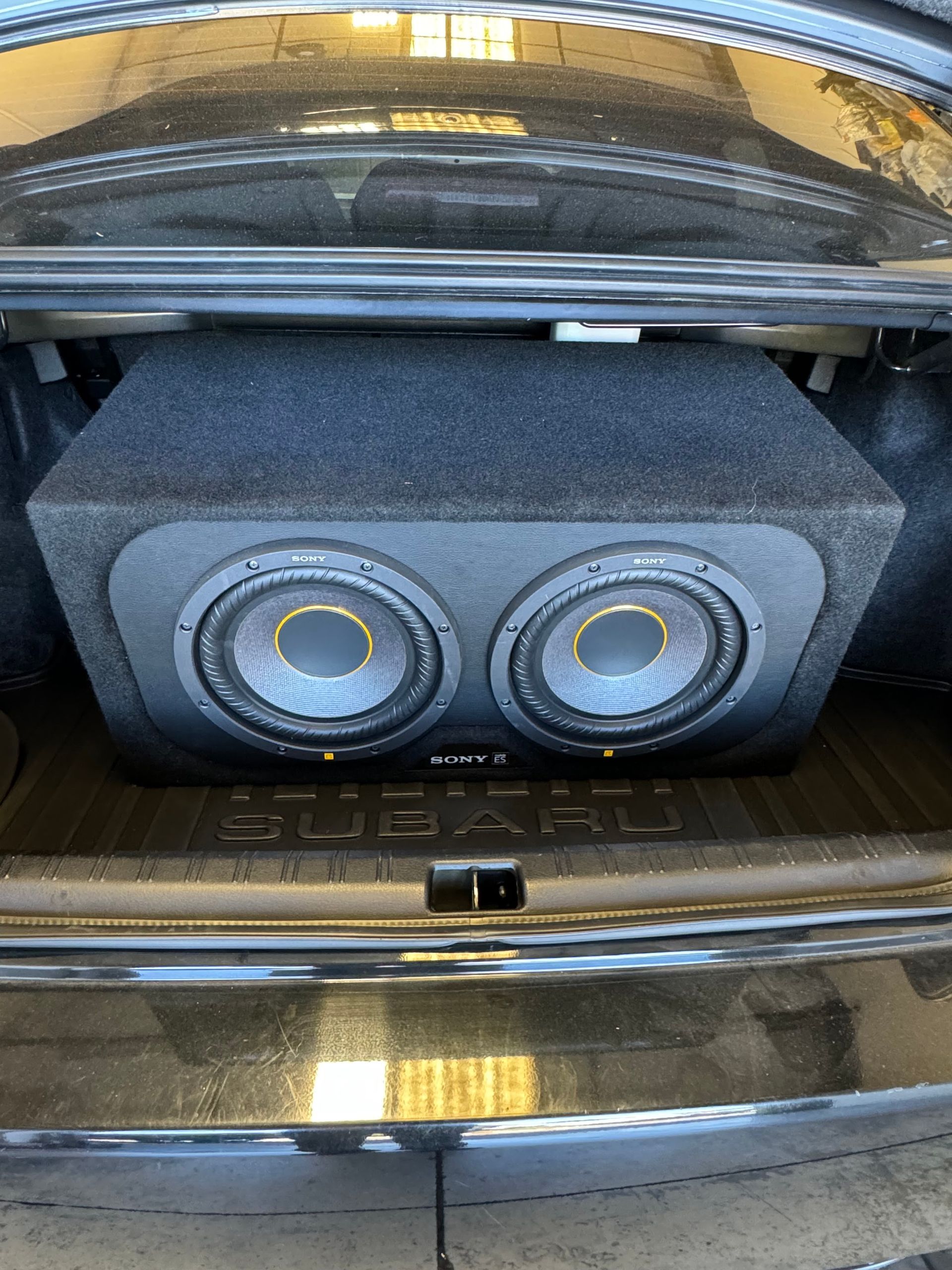 Two round speakers in a black box inside a car trunk
