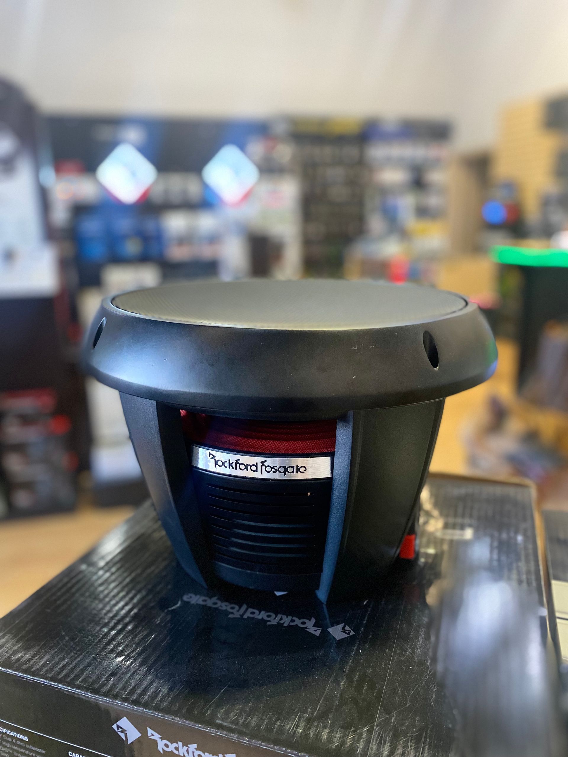 Black round speaker or subwoofer on a glossy tabletop in a blurred indoor setting